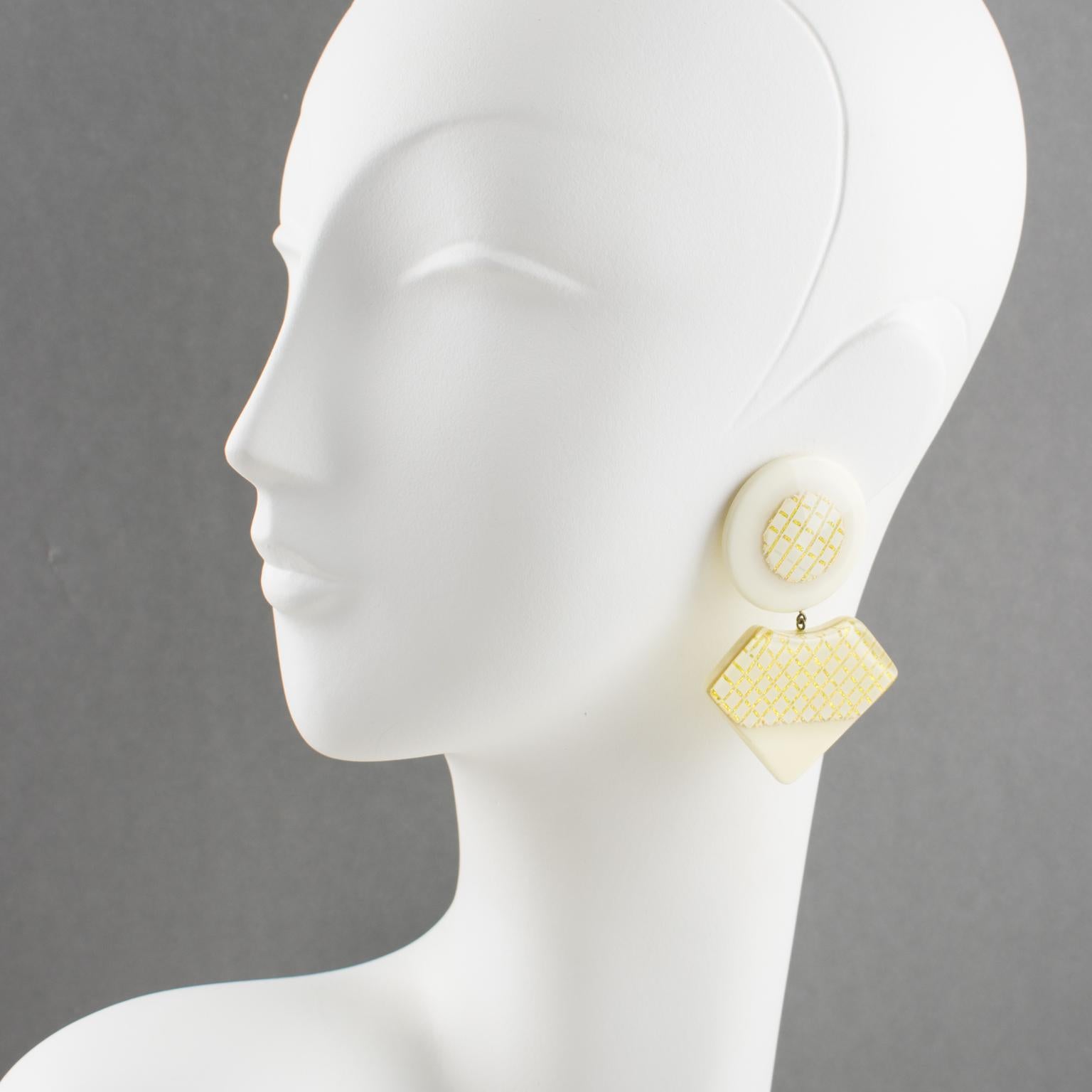 Lovely oversized Lucite clip-on earrings. Features geometric dangling elements in the cream-off-white color background with geometric gilt embedded design. There is no visible maker's mark.
Measurements: 1.94 in wide (4.9 cm) x 2.75 in high (7 cm).