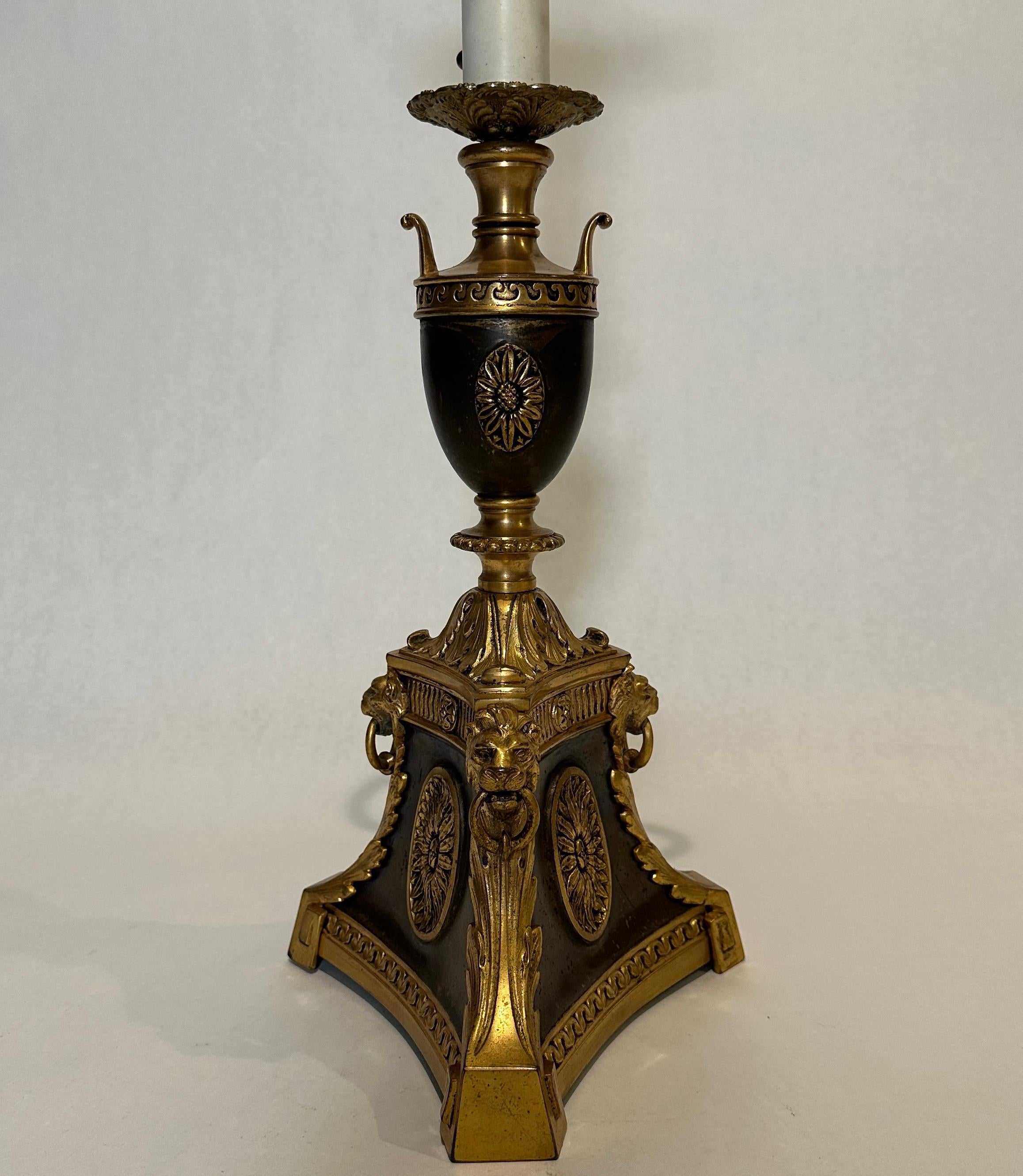 Fine quality gilt and patinated table or desk lamp. Elements include oval rosettes on the flat panels of a three sided base. Each corner with lion masks and acanthus leaves and two handled urn at top. Marked with original WM H. Jackson Company