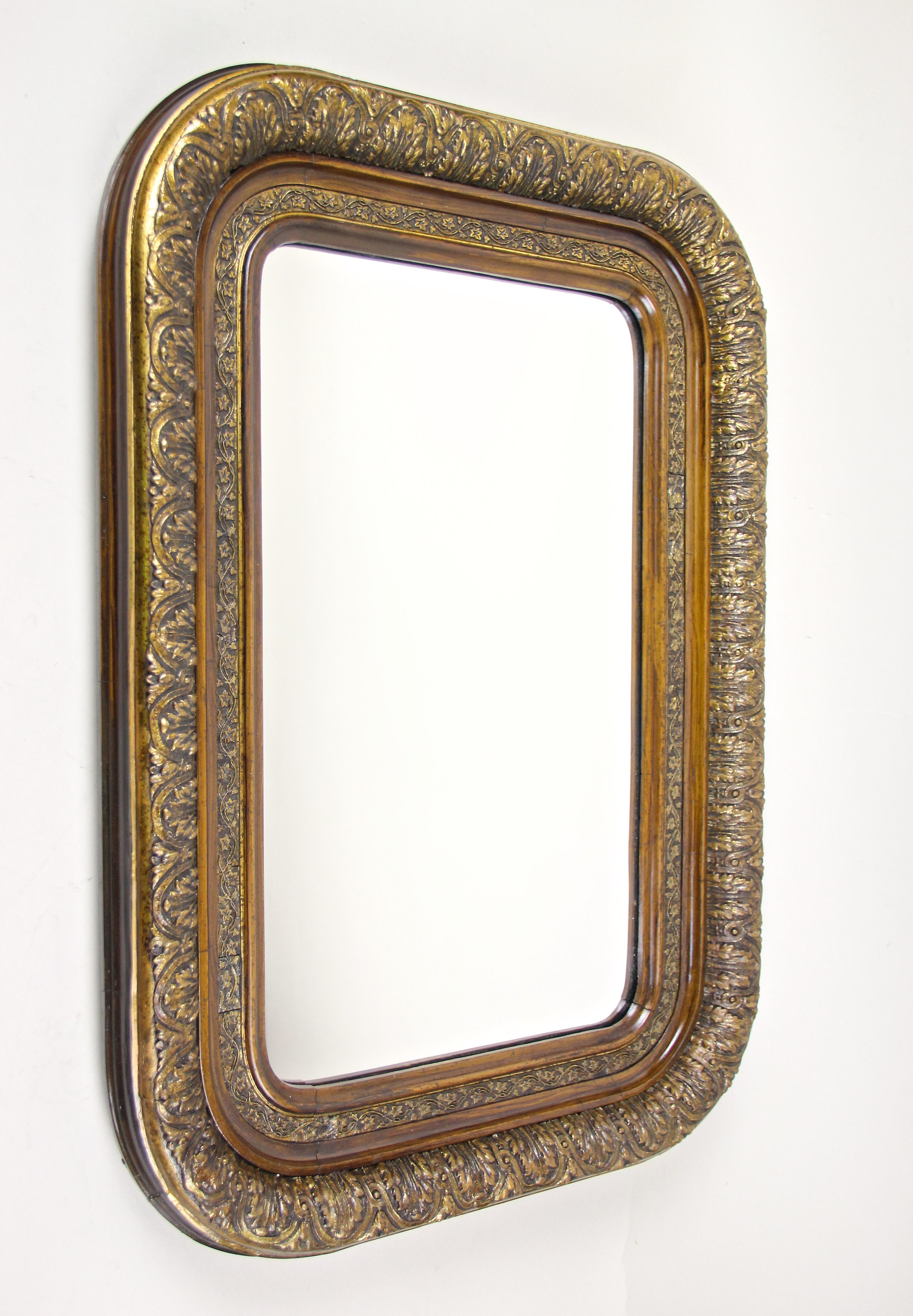 Exceptional gilt Biedermeier wall mirror with rounded corners from the period circa 1840 in Austria. Impressing with beautiful designed gilt stucco works and unusual wooden looking inner bars (these are also stucco but painted like wood!) this