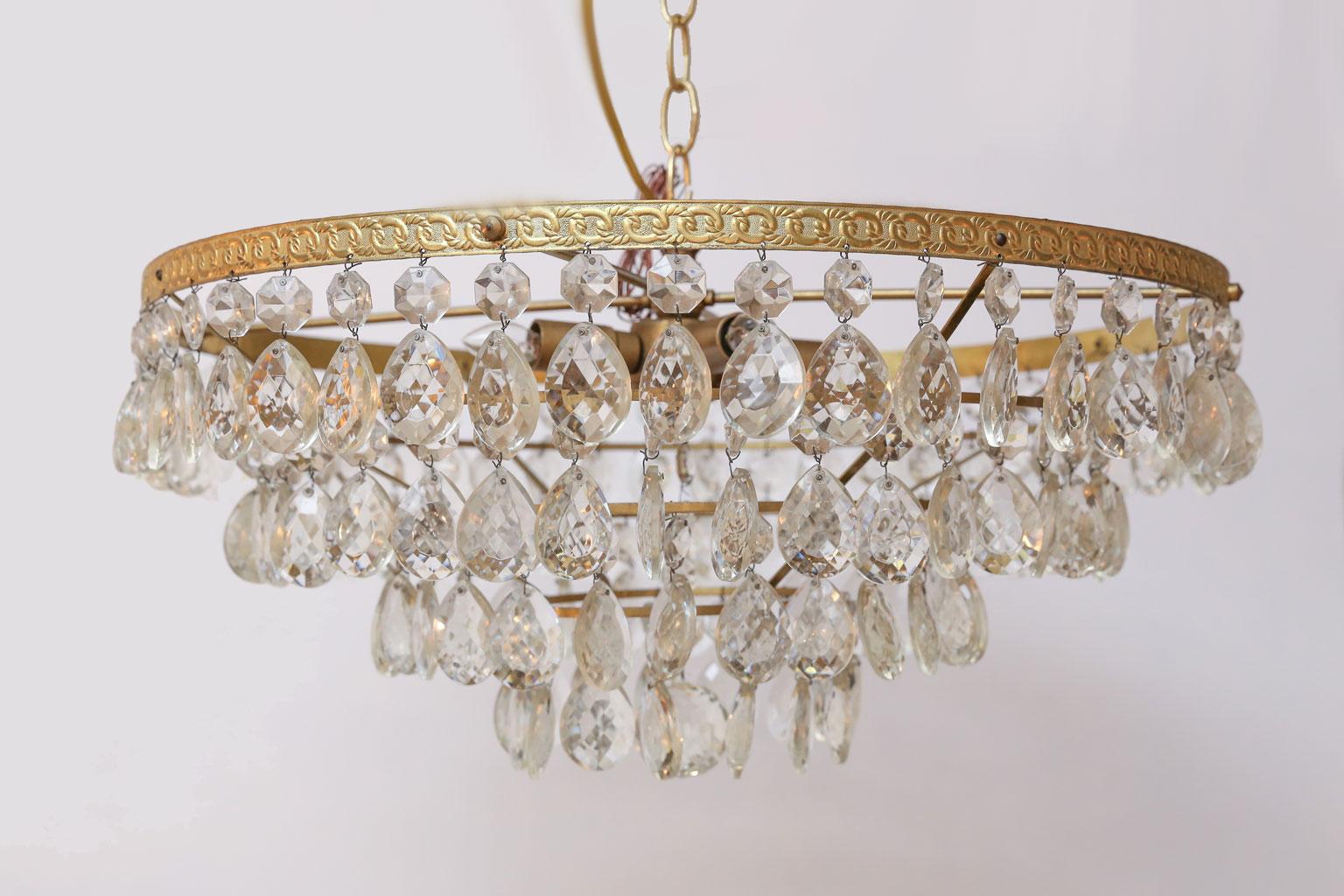 Gilt brass and crystal chandelier by Palwa in Germany. This mid-century modern, almost Hollywood Regency, chandelier can be modified to serve as a flush mount light. Crystal prism pendants are suspended from four tiers of cast gilt-brass rings.