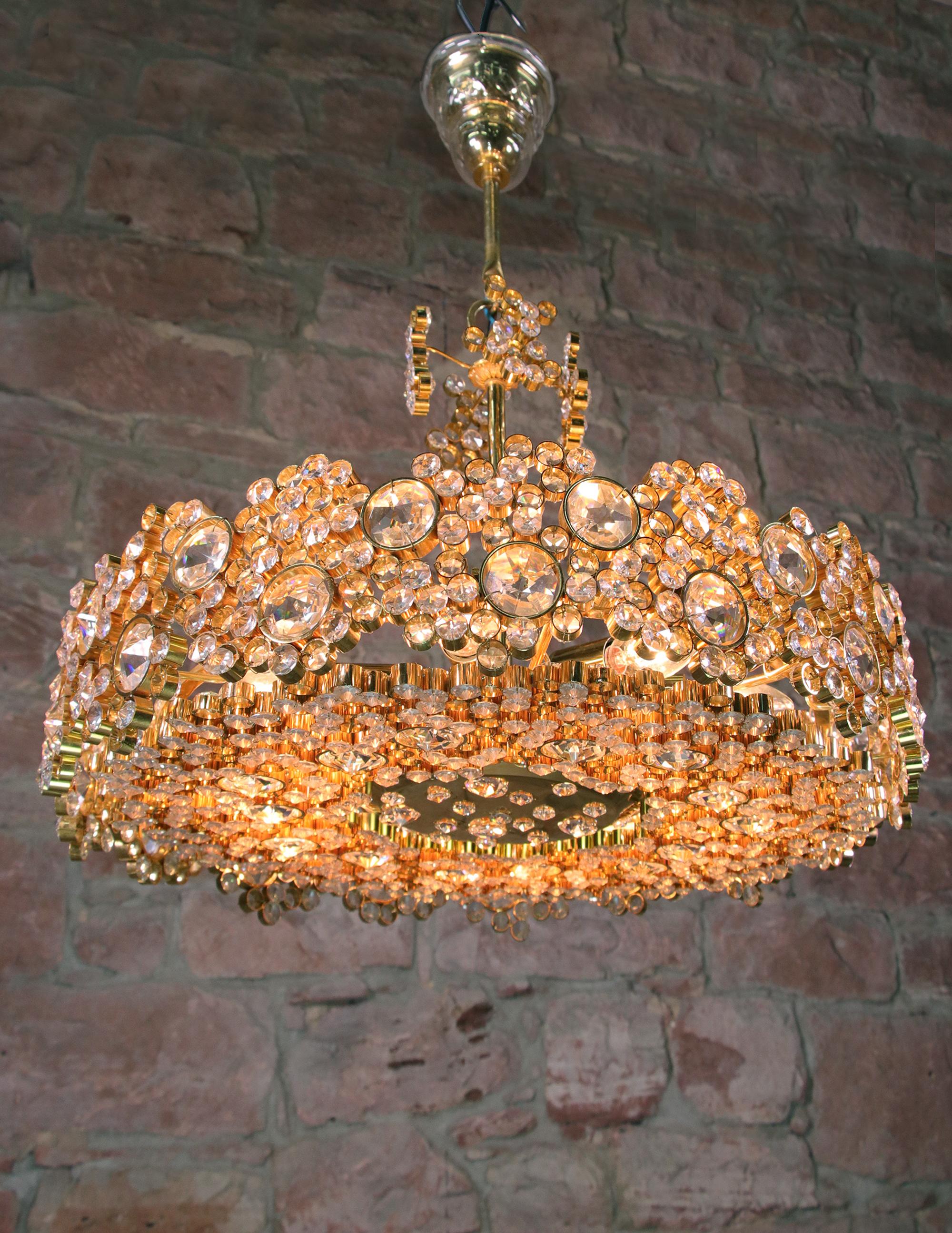 Glamorous crystal chandelier made of a 24-carat gold-plated brass frame with crystal prisms and gilt brass rings designed by Christoph Palme. Chandelier illuminates beautifully and offers a lot of light. Gem from the time. With this light you make a