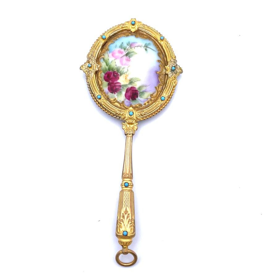 Beautiful antique gilt brass purse mirror.  The center is porcelain, decorated with a vibrant enamel depiction of red, pink and yellow roses.  Bordered by gold leaf applique.  Set in a gilt frame, with a reed and bead pattern. Accented with ten