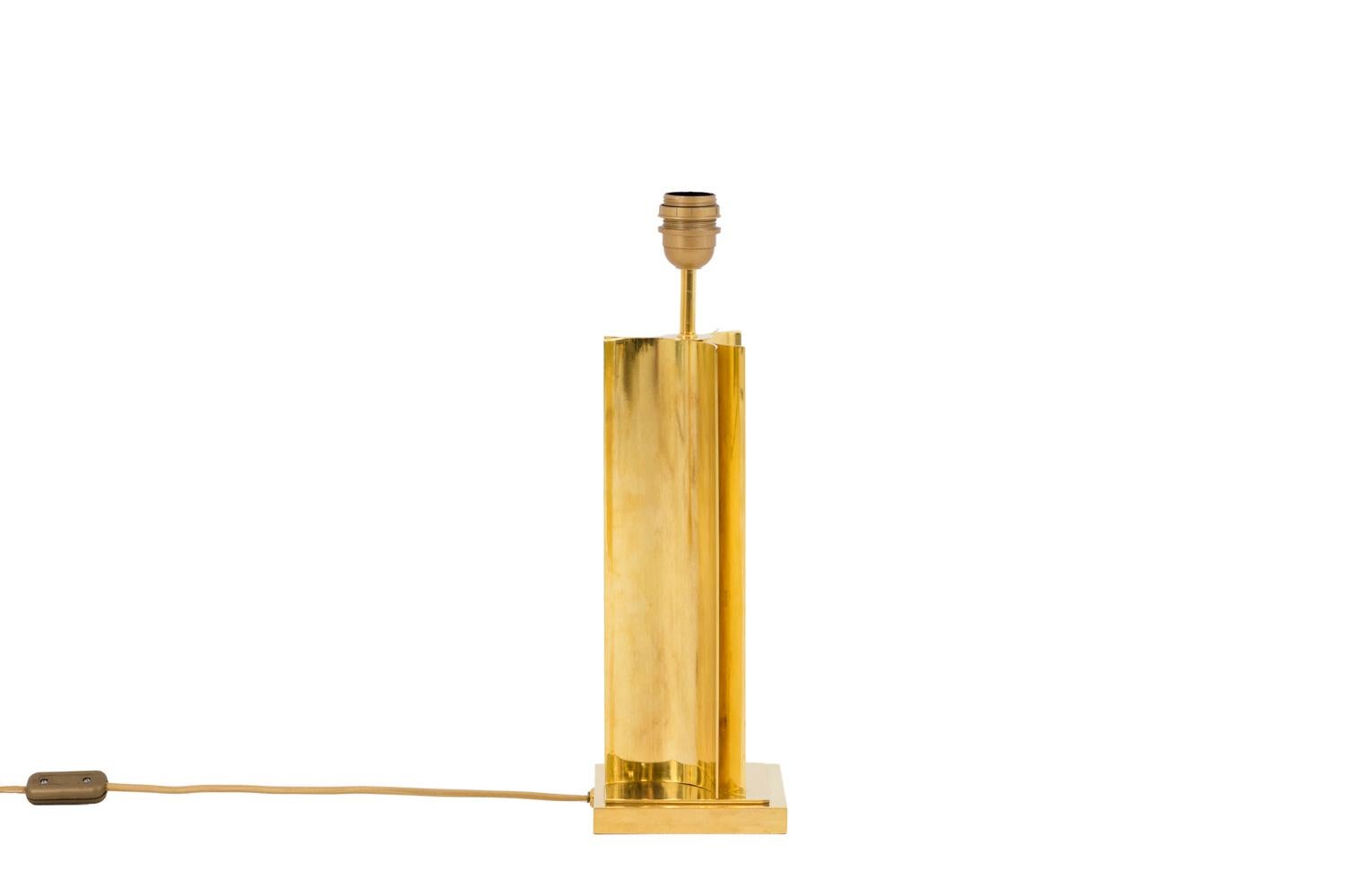 Lámpara de latón dorado con fuste en forma de tres medios tubos apoyados alrededor de un palo redondo central.
Base moldeada de forma cuadrada.

Pantalla cuadrada de organza blanca.

Obra realizada en la década de 1970.

Sistema eléctrico