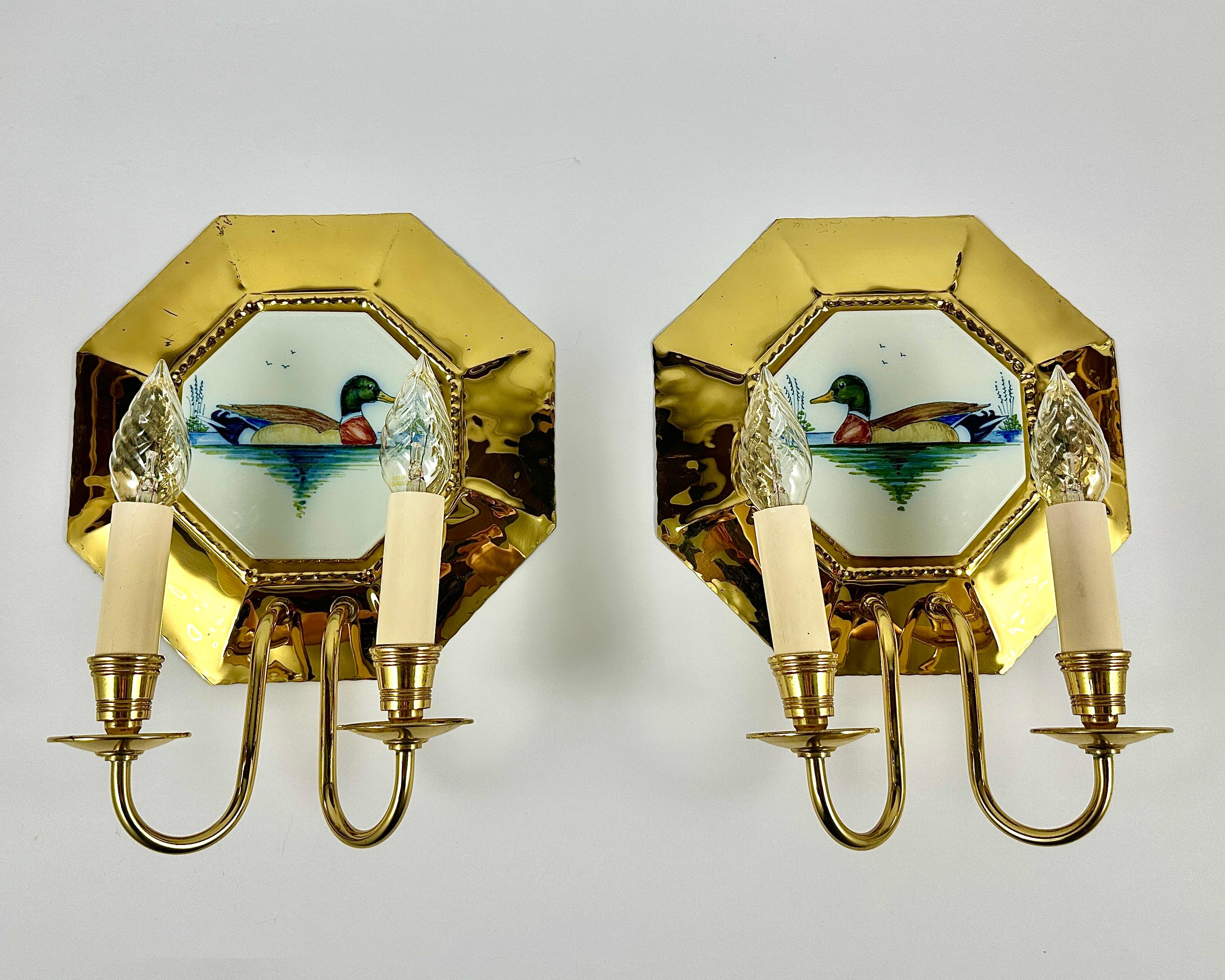 Wall sconces consisting of a porcelain plate on a brass base.

These vintage sconces are in neoclassical style, with a classic design and traditional casting techniques.

Two brass anrms extend from the bottom of each base. At the top of each arm is