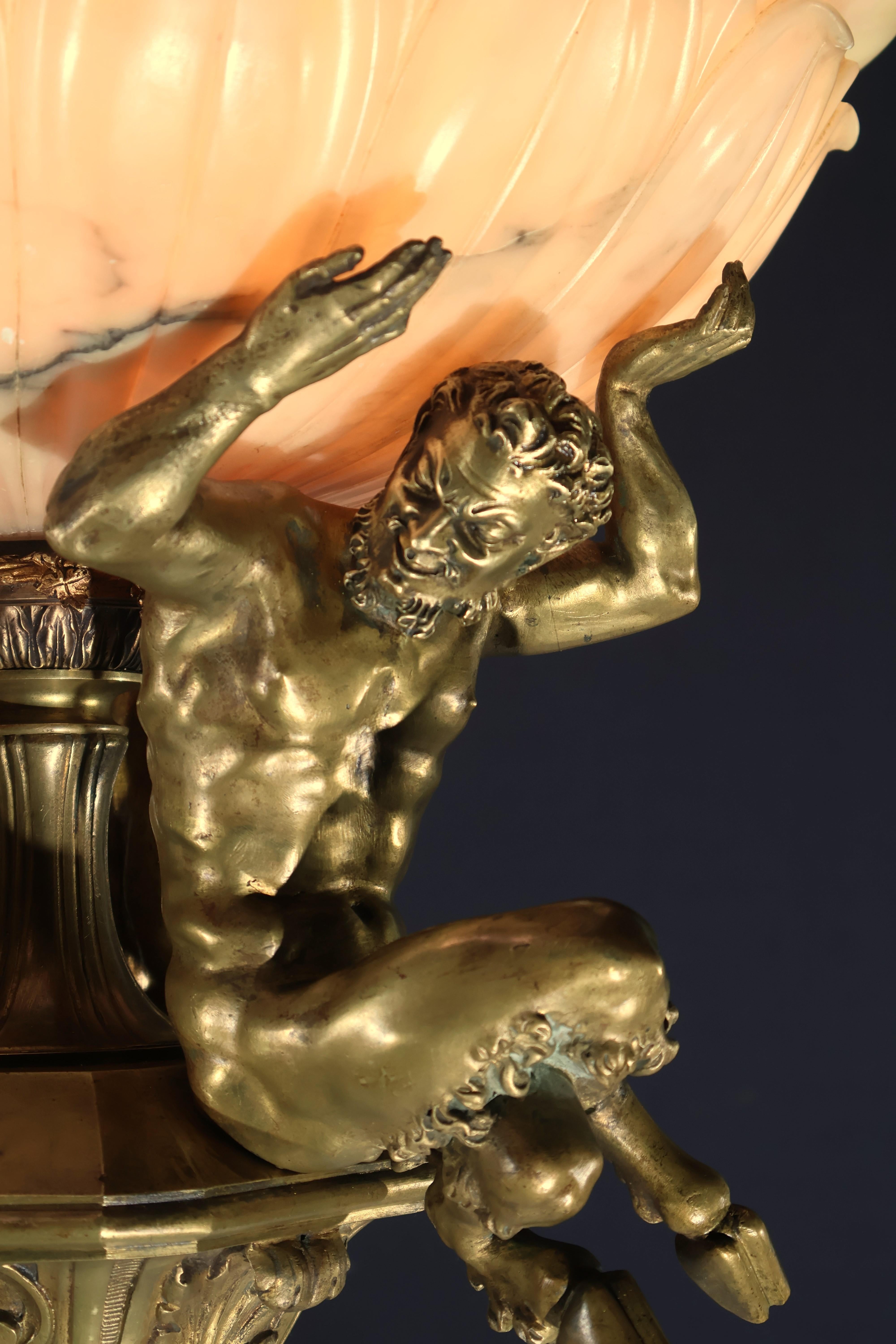 Un insolito lampadario in bronzo dorato con tre satiri seduti che sorreggono una cupola di alabastro riccamente intagliata. Francia, circa 1910. 6 luci. 
Dimensioni: Altezza  23