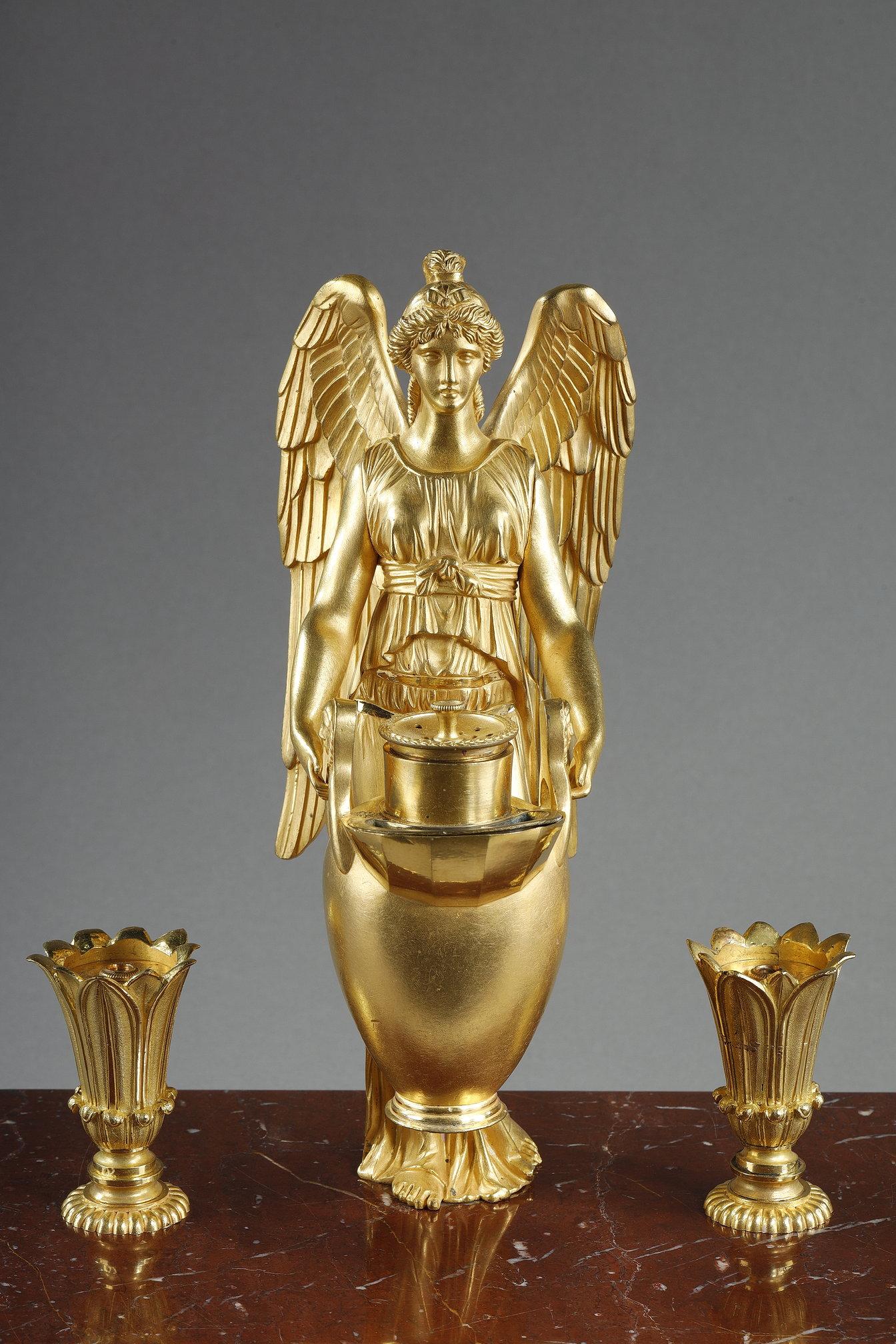 Elegant Empire-period inkwell featuring a rectangular base in griotte red marble, embellished with gilded bronzes. The main decoration, of great finesse, represents a winged figure in chased and gilded bronze carrying a vase, surrounded by two