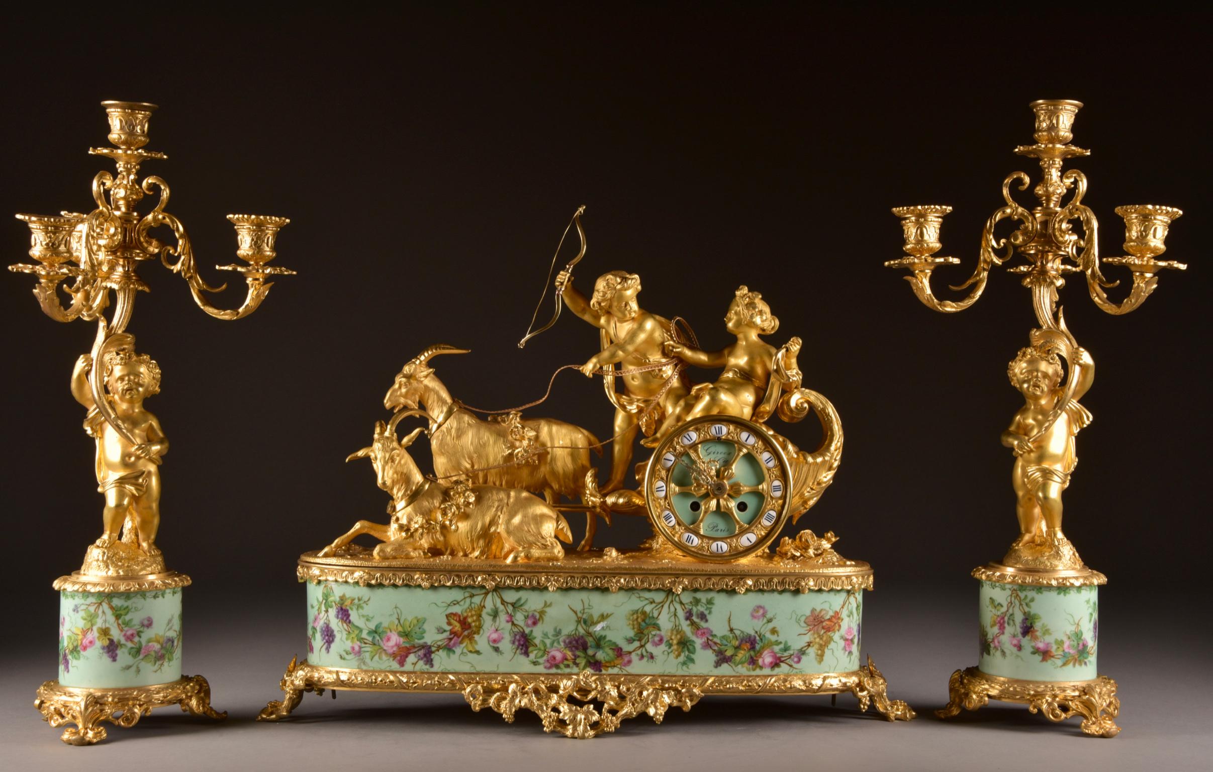 Very prestigious clock, and a pair of three-light candelabras by: Alphonse Giroux & Cie, 1855, made of fire-gilt bronze and romantic porcelain. Rare chariot surmounted by two putti on a goat-driven chariot. The time piece stamp is from: Japy Frères