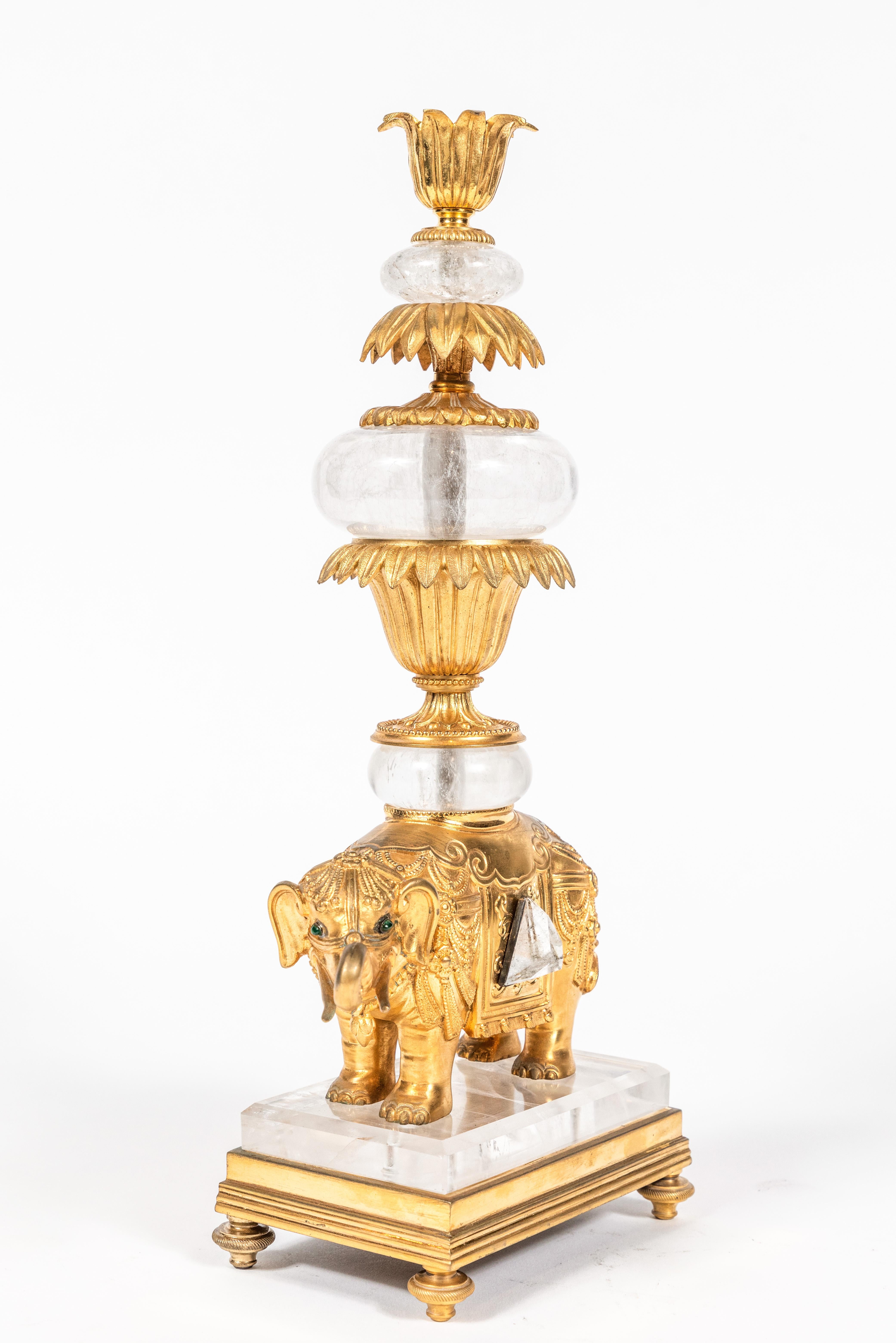 A glittering, beautifully detailed, candlestick featuring a gilt bronze elephant bearing a tiered, floral candlestick with alternating layers of polished rock crystal. The elephant has emerald eyes, and the body is decorated throughout with raised