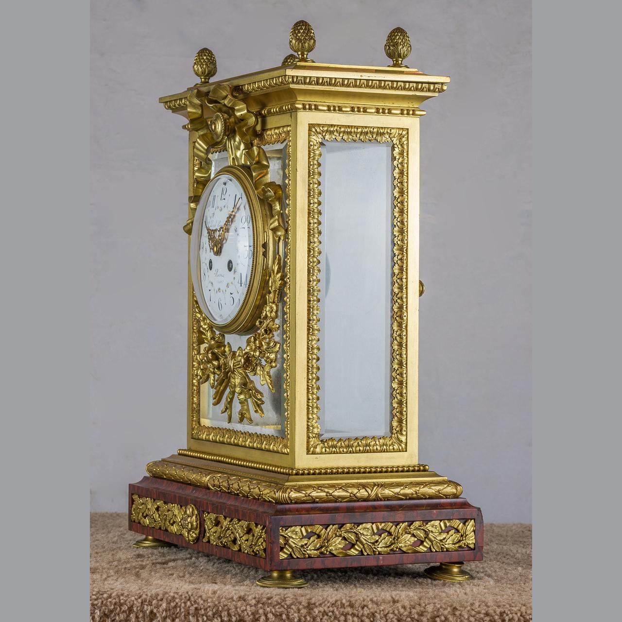 Surmounted by berry finials, the beveled glass sides within cast leaf-tips borders mounted on the front with a ribbon tied enamel dial inscribed, “Paul Graselins/Auriel Charlot 8,” above a wreath. The movement stamped, “Lemerle Charpentier Fabrizue