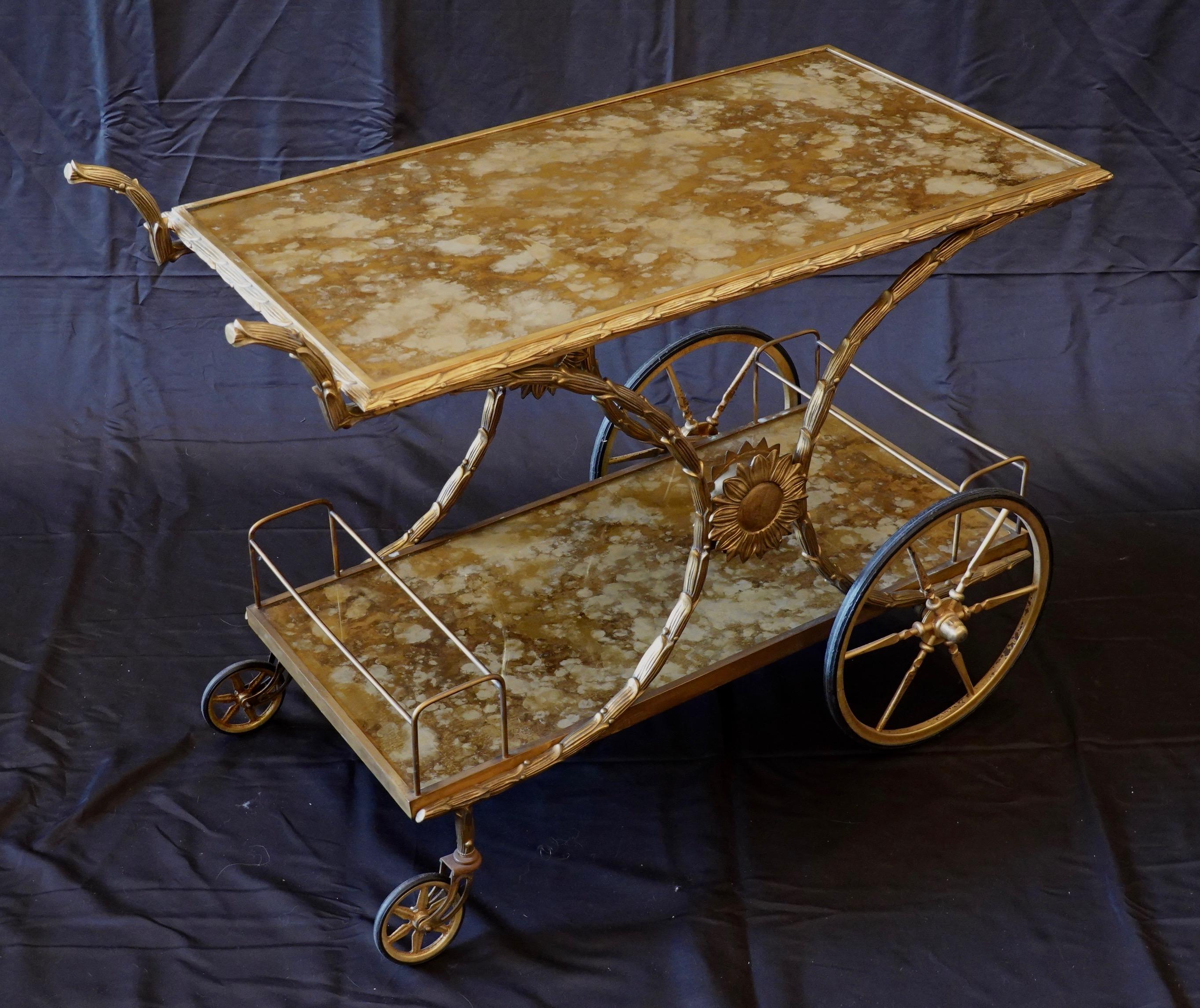 A highly-decorative and very rare French gilt-bronze bar cart with a gold églomisé tops. The bronze frame is in the form of palm leaves, and sun flowers adorn the sides where the supports come together.