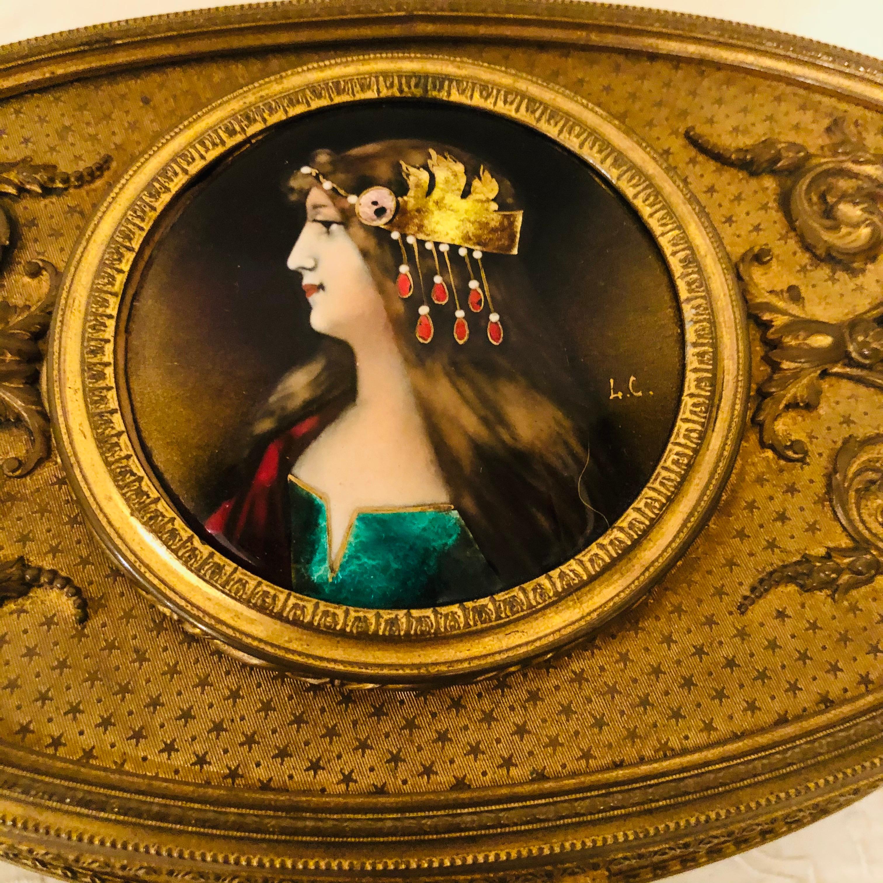 Bronze box with an enamel artist signed portrait of a beautiful lady on four raised feet. It is artist signed L. C. The box has a rose velvet interior. It is from the late 19th century. It is 10.5 inches wide, 7 inches deep and 3.5 inches tall. It