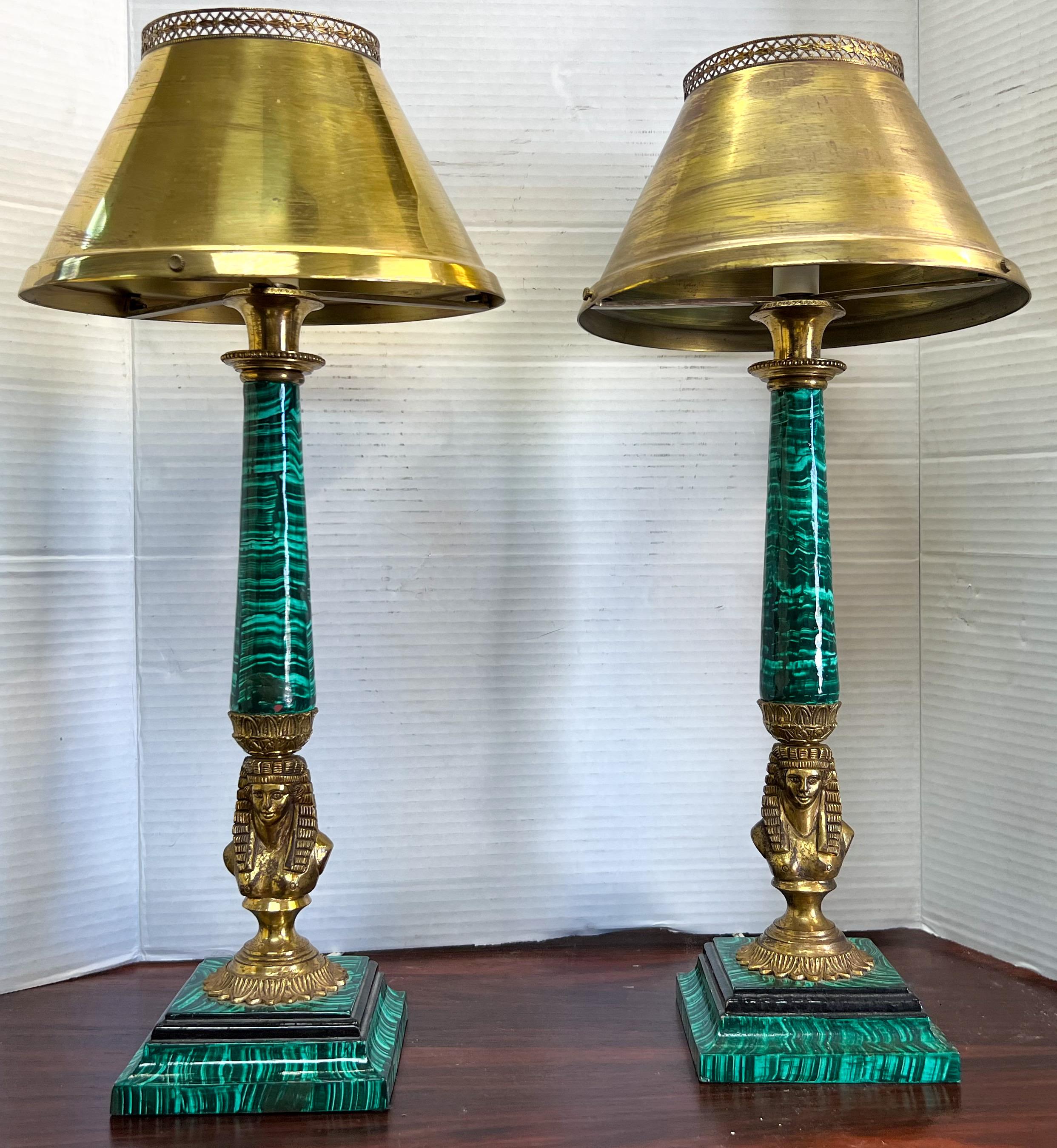 These are a showstopper! This is a pair of Egyptian revival style table lamps. The pharaoh at the base is gilt bronze. The stems are hand painted with a faux malachite finish. The shades are brass and do show a bit of wear. They are in working order.