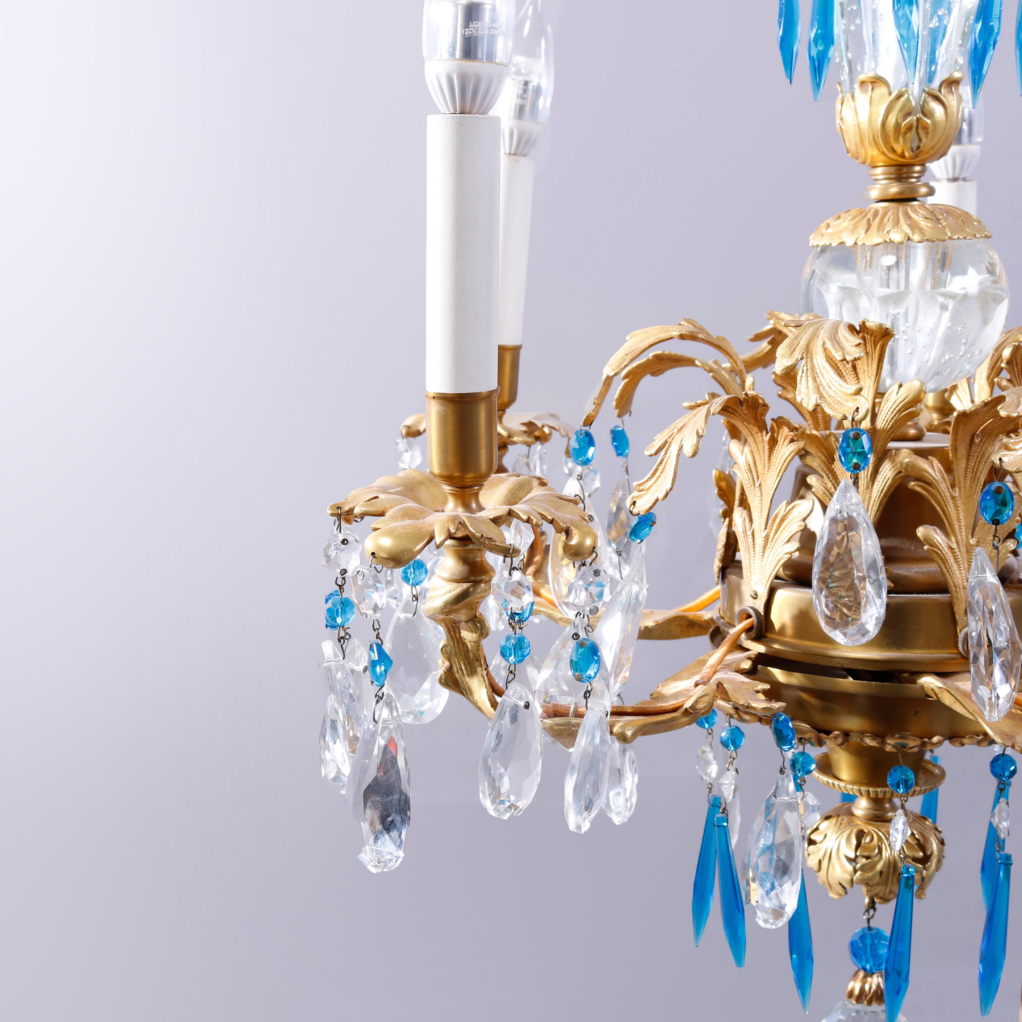 A French Louis XIV style chandelier in the manner of Baccarat offers gilt bronze and brass frame with central crystal insert and scrolled foliate form arms terminating in candle lights, drop and strung blue and colorless crystals throughout,
