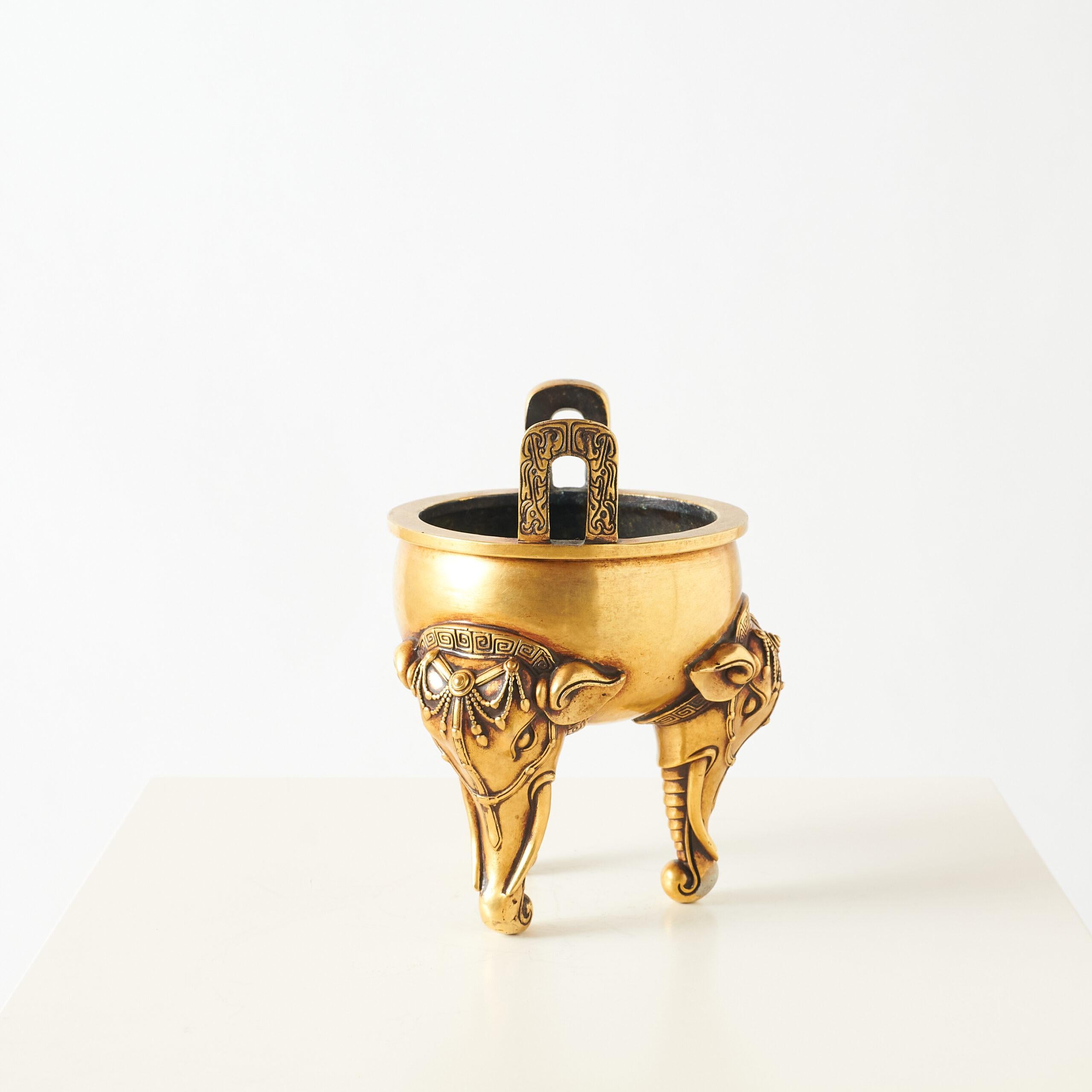 Gilt Bronze Censer with Elephant-Form Legs

Bronze incense burner with a tripod base featuring elephant head legs and trunks as feet. The round body has two upright handles and is decorated with detailed carvings. Finished in a warm gilt tone.

The