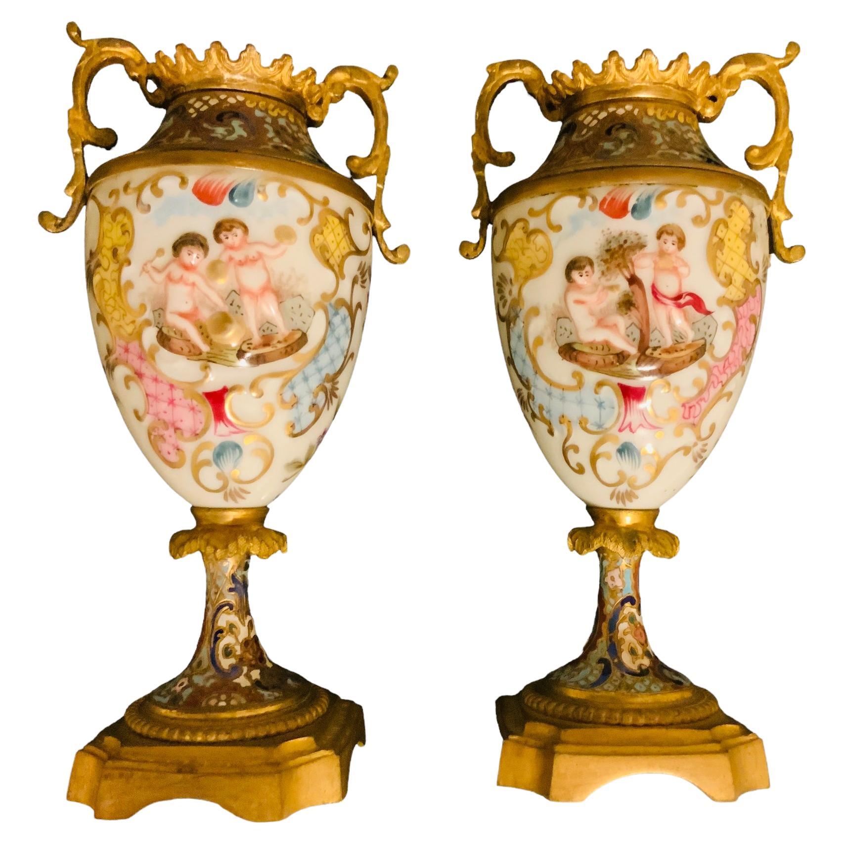 This is a pair of Champleve and Capodimonte porcelain small urns. It depicts a pair of urns with colorful champleve pattern of flowers and scrolls at the neck, shoulder and feet area. The body of the urn is made of porcelain and decorated with a