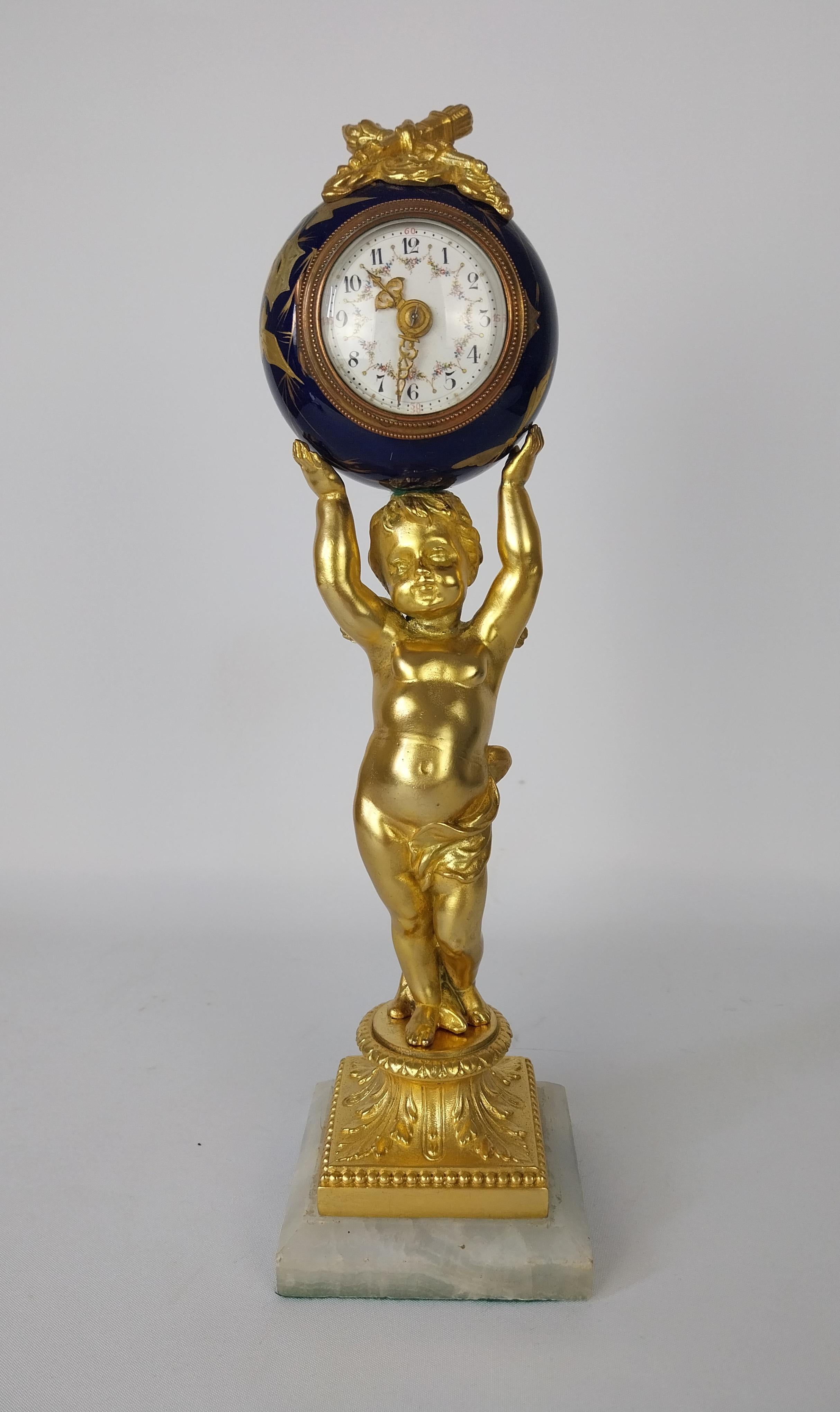 Manteluhr im Stil Ludwigs XV1 mit weißem Porzellanzifferblatt, Plattformhemmung in rundem, mit Bleu du roi dekoriertem Gehäuse, das von einer vergoldeten Putte auf einem Alabastersockel gehalten wird. 
Vollständig gewartet und in perfektem