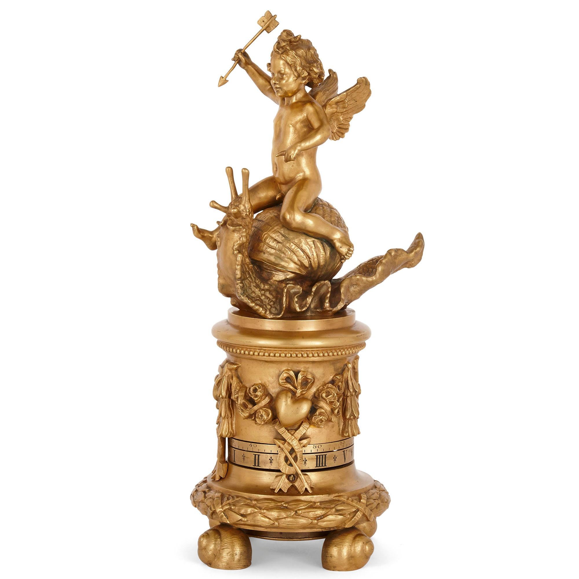 Gilt bronze cylindrical mantel clock with emblems of love
French, 19th century
Measures: Height 40cm, diameter 17cm

This fabulously quirky mantel clock is modelled to depict Cupid (or Eros), the god of Love, holding his love arrow and sat atop