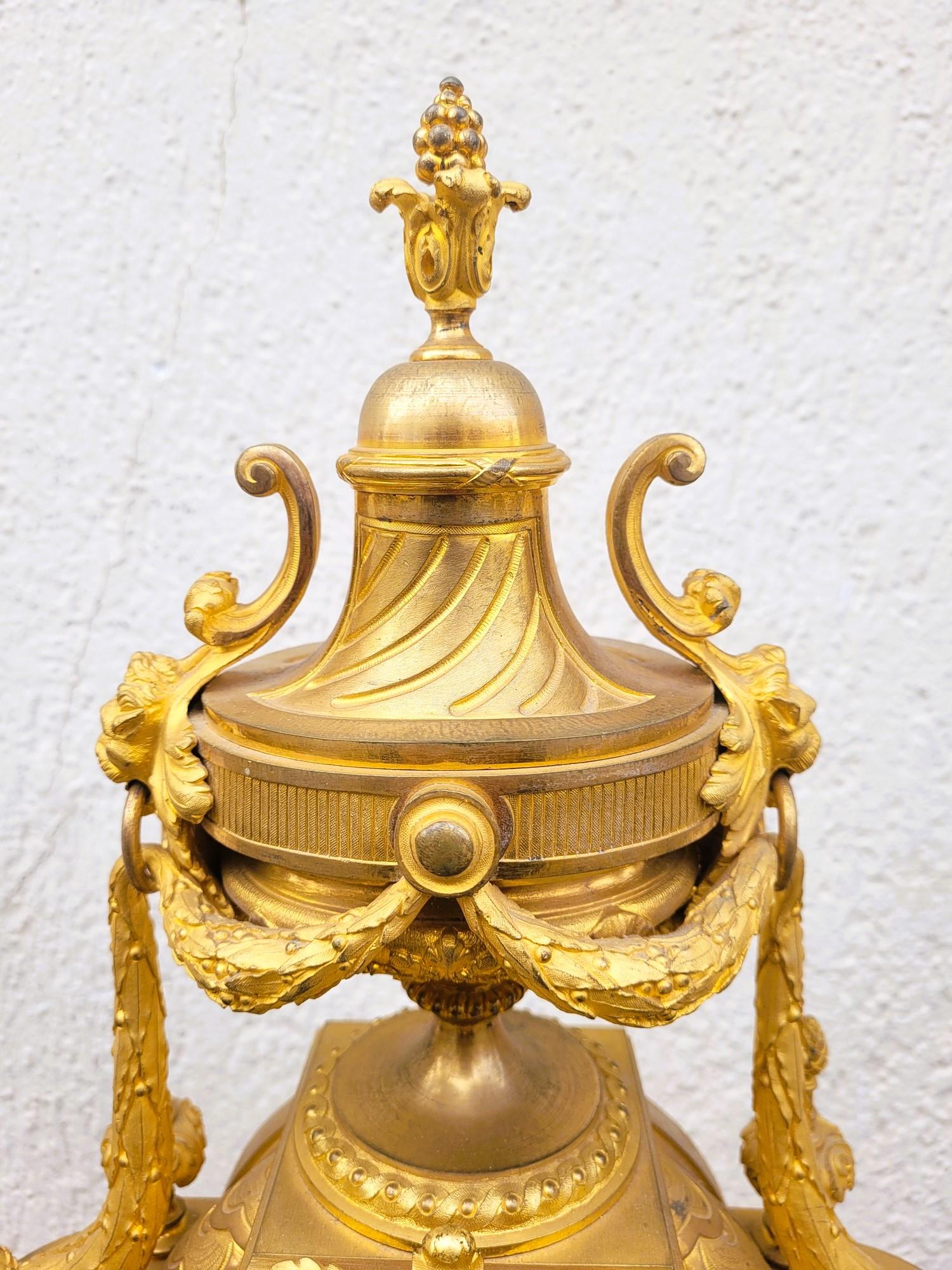 Gilt bronze mantelpiece with 2 patinas (matt and shiny) composed of a clock and 2 candelabras. 

The clock is decorated with caryatids holding garlands of flowers and laurel leaves, and fire pots or basins with pines and lion heads.   
The