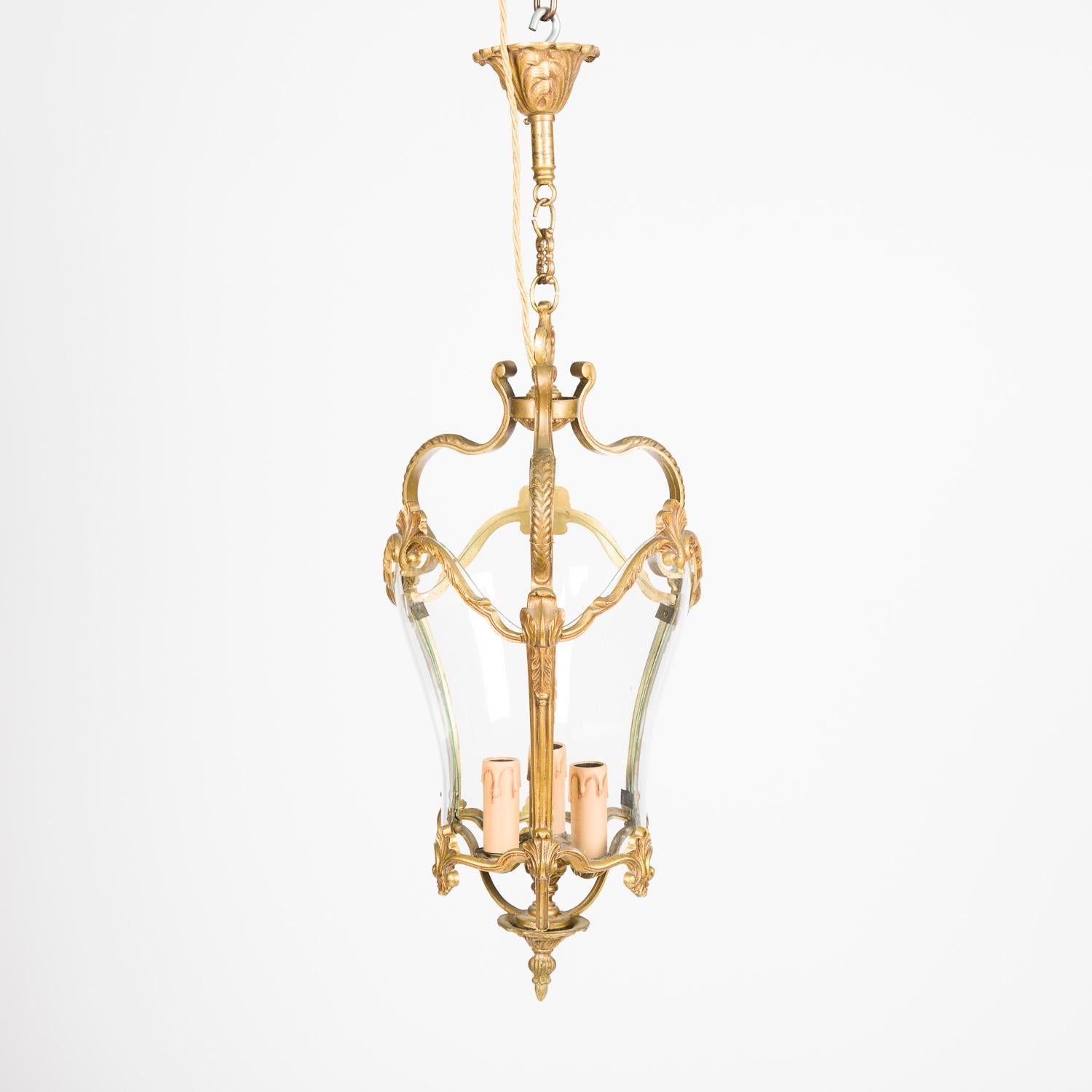 A gilt bronze bow glass glazed lantern decorated with scallop and rope twist motifs, in the Louis XV style, French, circa 1925.

With 3 internal light fittings, ceiling rose and chain.

Re-wired and tested.

Height of lantern: 20.5 inches - 52