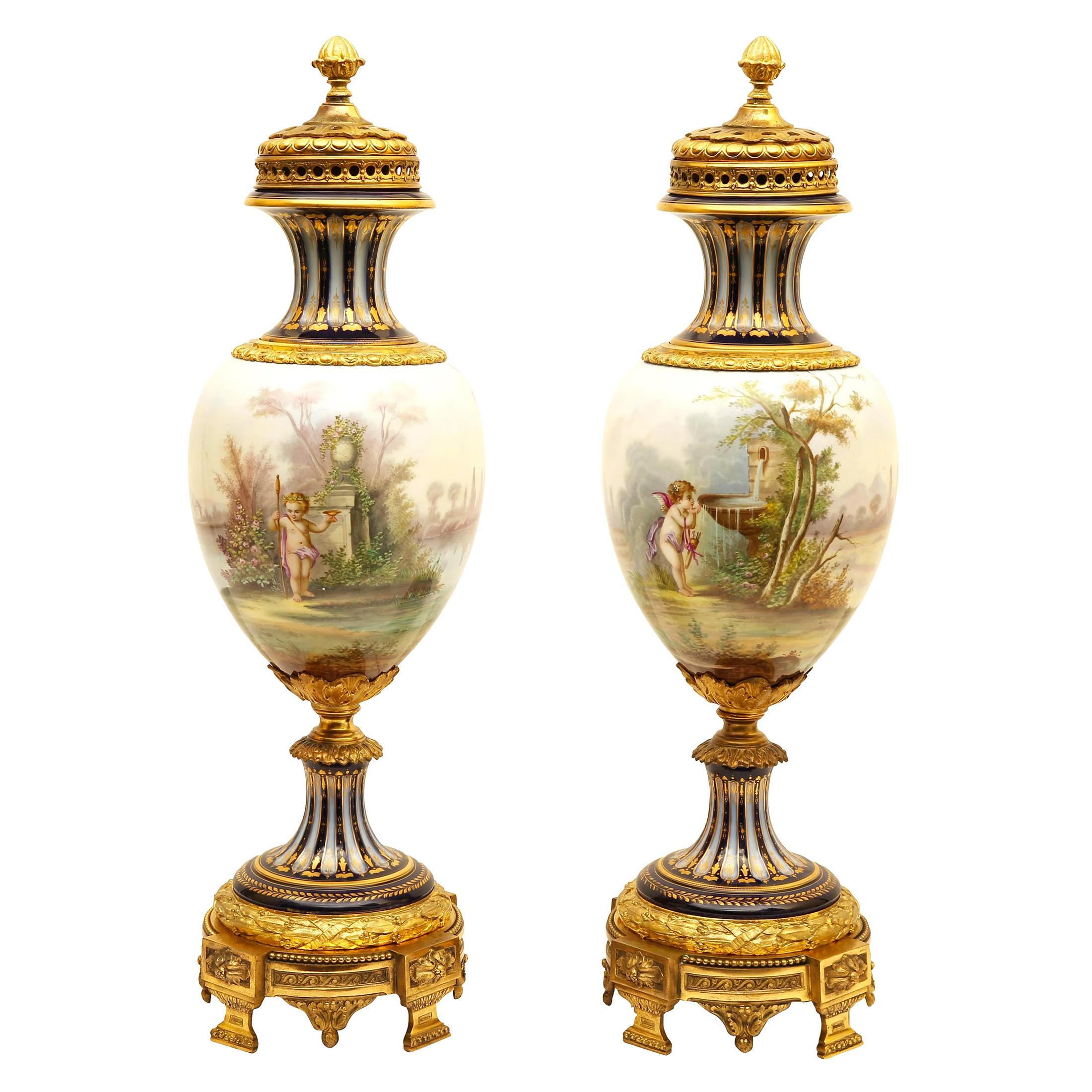 A fine quality elegant pair of bronze mounted Amphora shaped Sèvres style polychrome enamel glazed and decorated foot and covered porcelain vases. The ovoid shaped vases with a summer landscape genre scene of women and putti. a cobalt blue ground