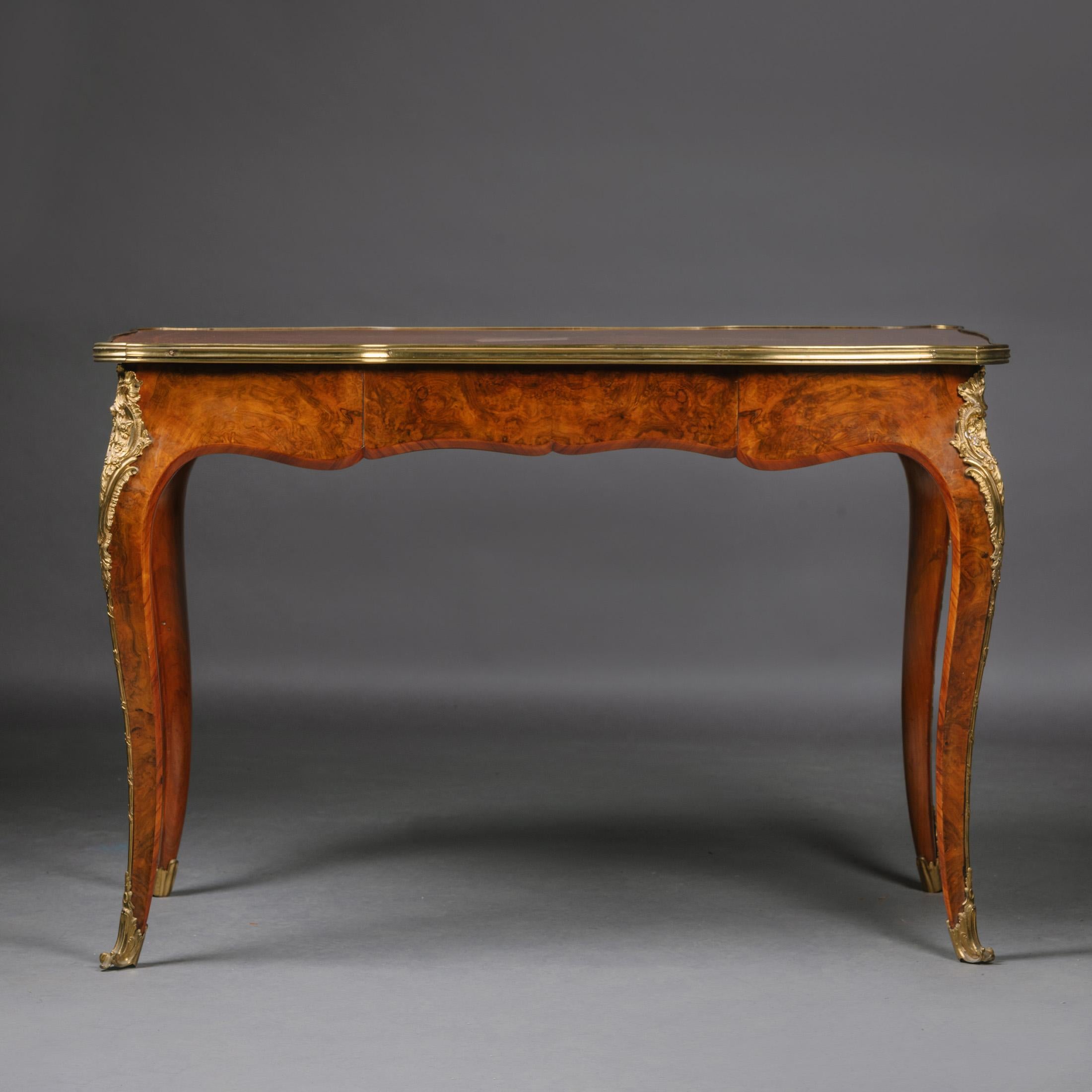 A Gilt-Bronze Mounted Burr Walnut Writing Table, Probably by Gillows. 

The rectangular top has a gilt-bronze surround above a serpentine frieze fronted by a central drawer. The corners have foliate claps above cabriole legs.

England, circa 1850.
