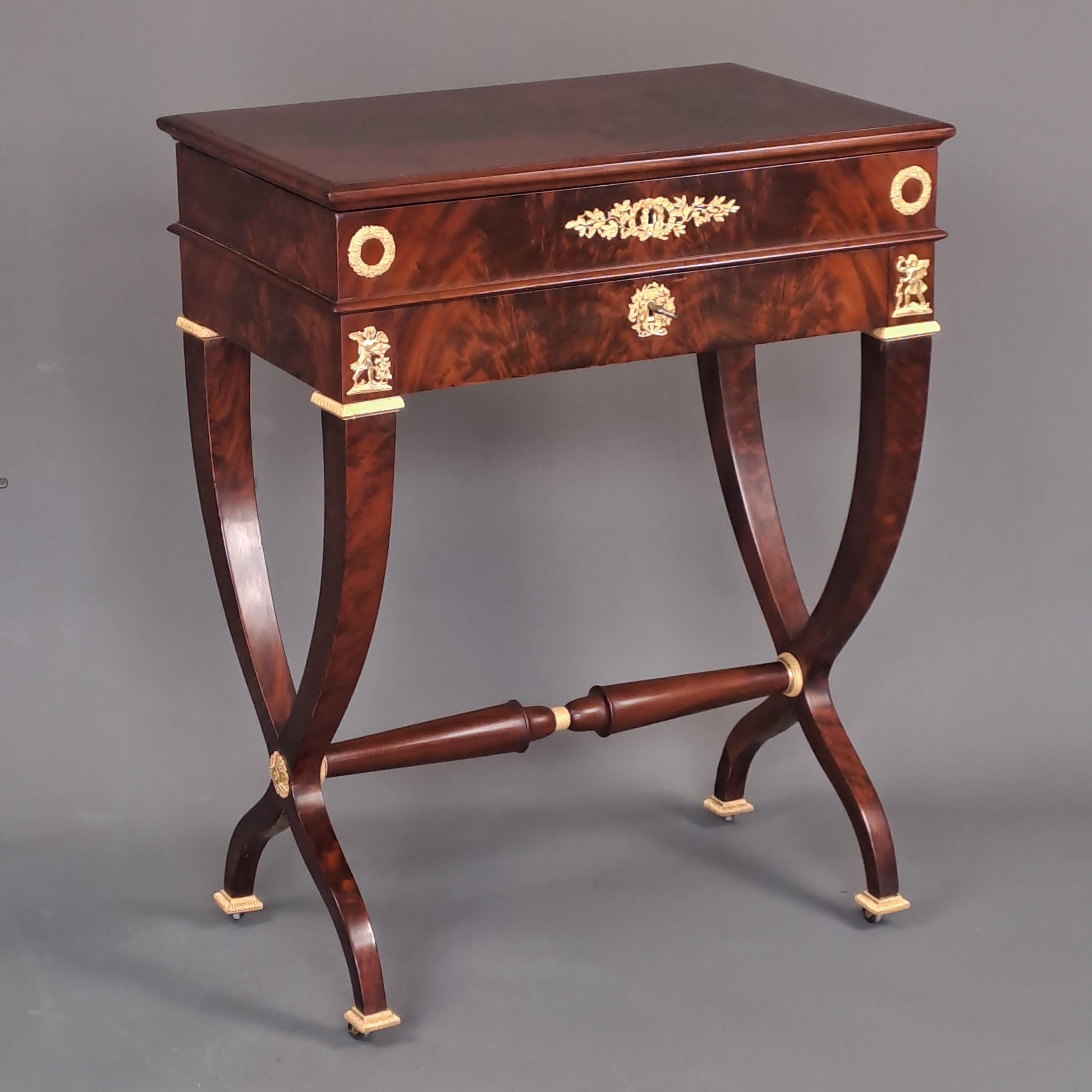 Empire period work table in flamed mahogany and gilt bronze mounted.
Magnificent table forming writing desk and work table. The drop-leaf top features a recessed mirror, storage compartments, as well as a removable candle holder and pin