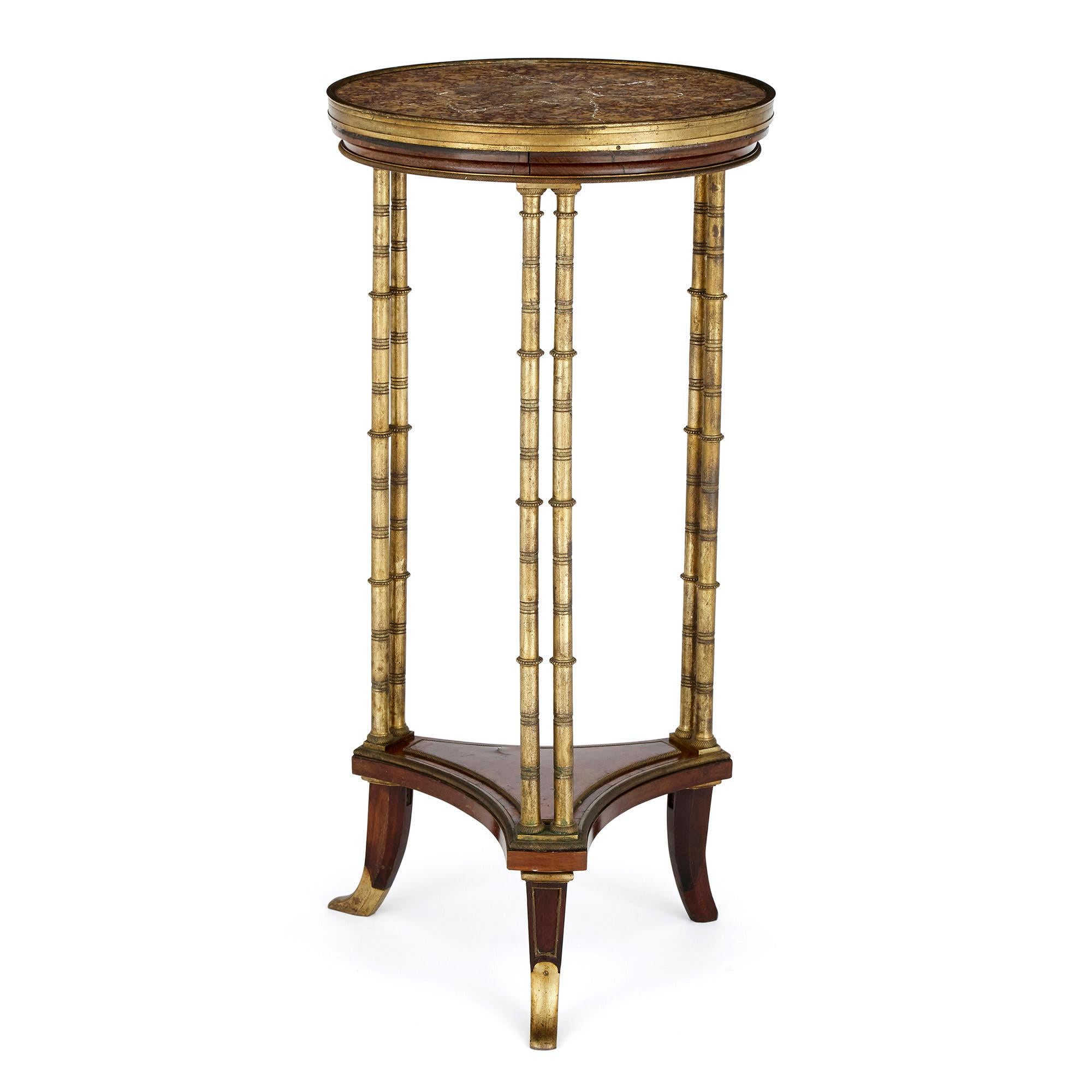 Cette table d'appoint circulaire d'Henry Dasson est surmontée d'un plateau en marbre incrusté, délimité par un anneau en bronze doré et placé au-dessus d'un tablier en acajou. La table repose sur trois pieds à deux colonnes en bronze doré, qui