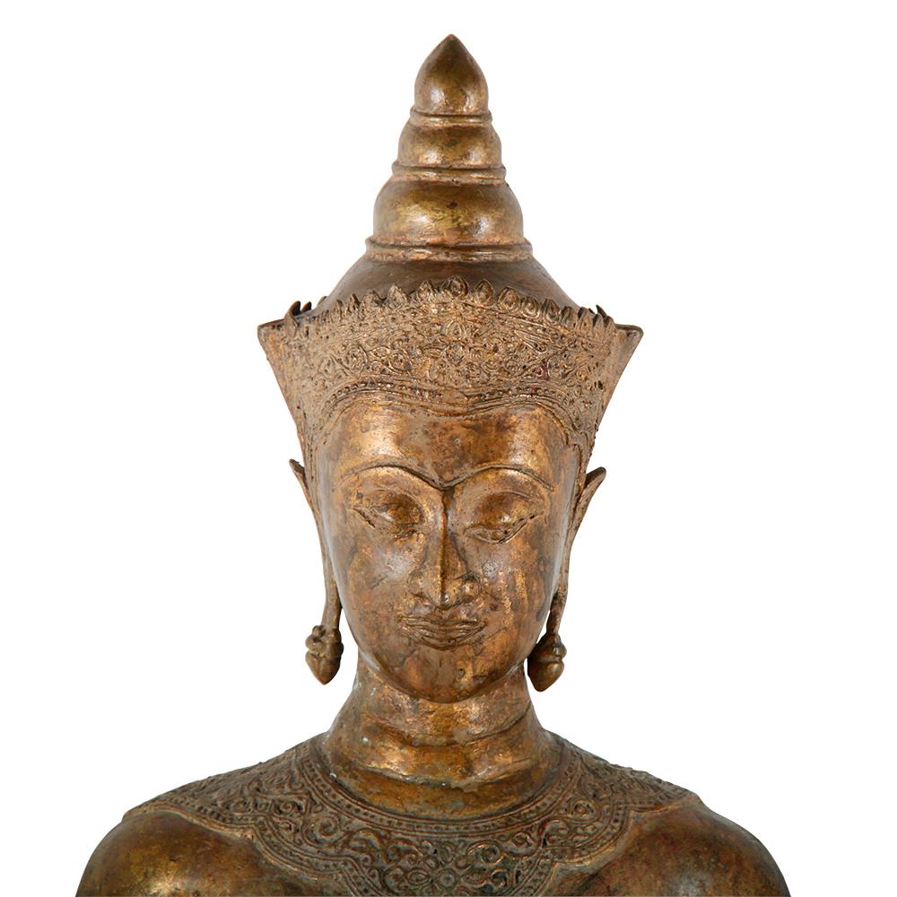 A Thai standing Buddha in gilt bronze and gesso embellished throughout with ornate applied detailing. Standing in a “repelling” pose, with both palms facing forward, said to have been based either on a story of stopping a great flood, or stopping