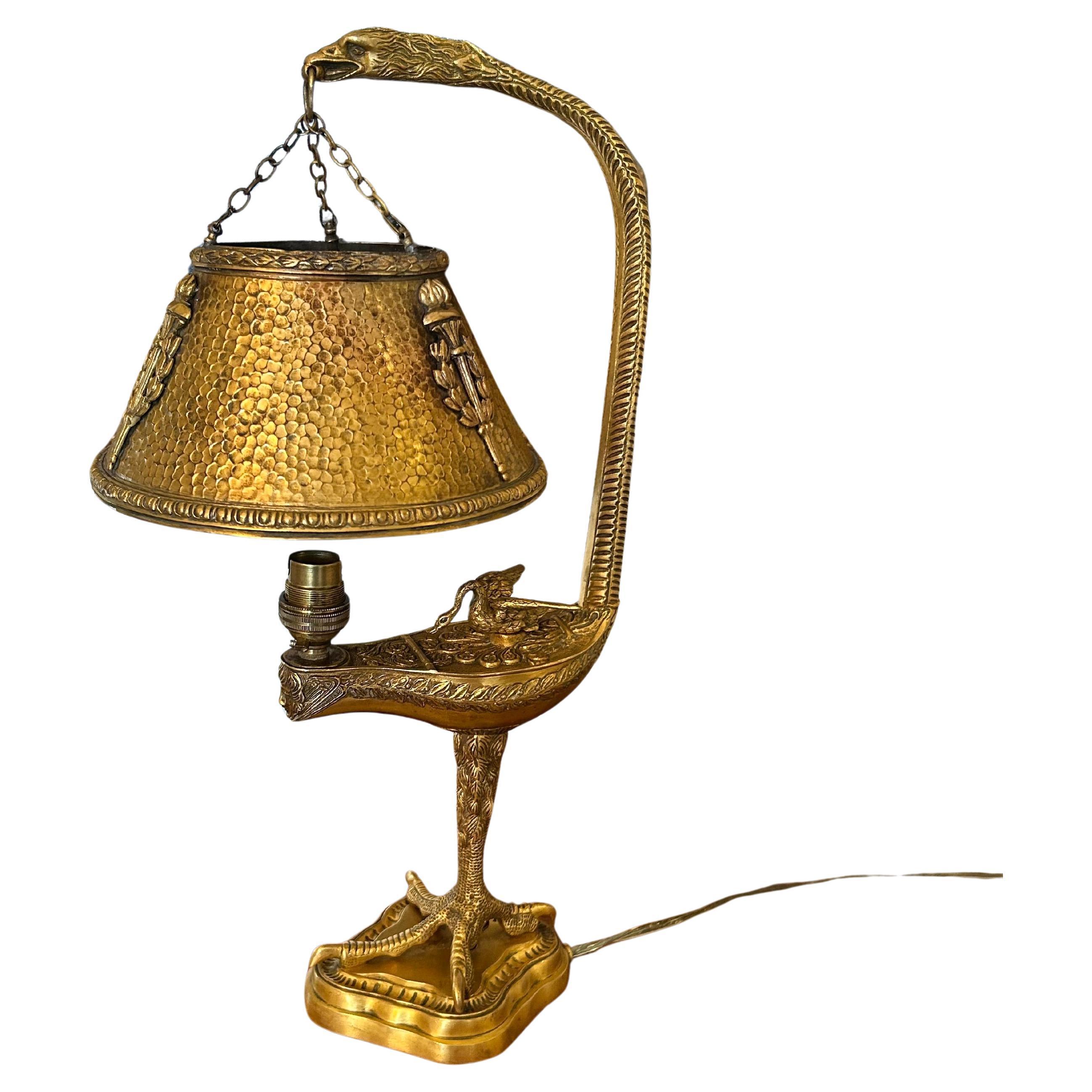 This is an incredibly unique, Empire, gilt bronze lamp, most probably French and from the late 19th century. The lamp has a lantern shape with a claw foot base and an elongated swan holding the hammered bronze shade. Beneath the shade another