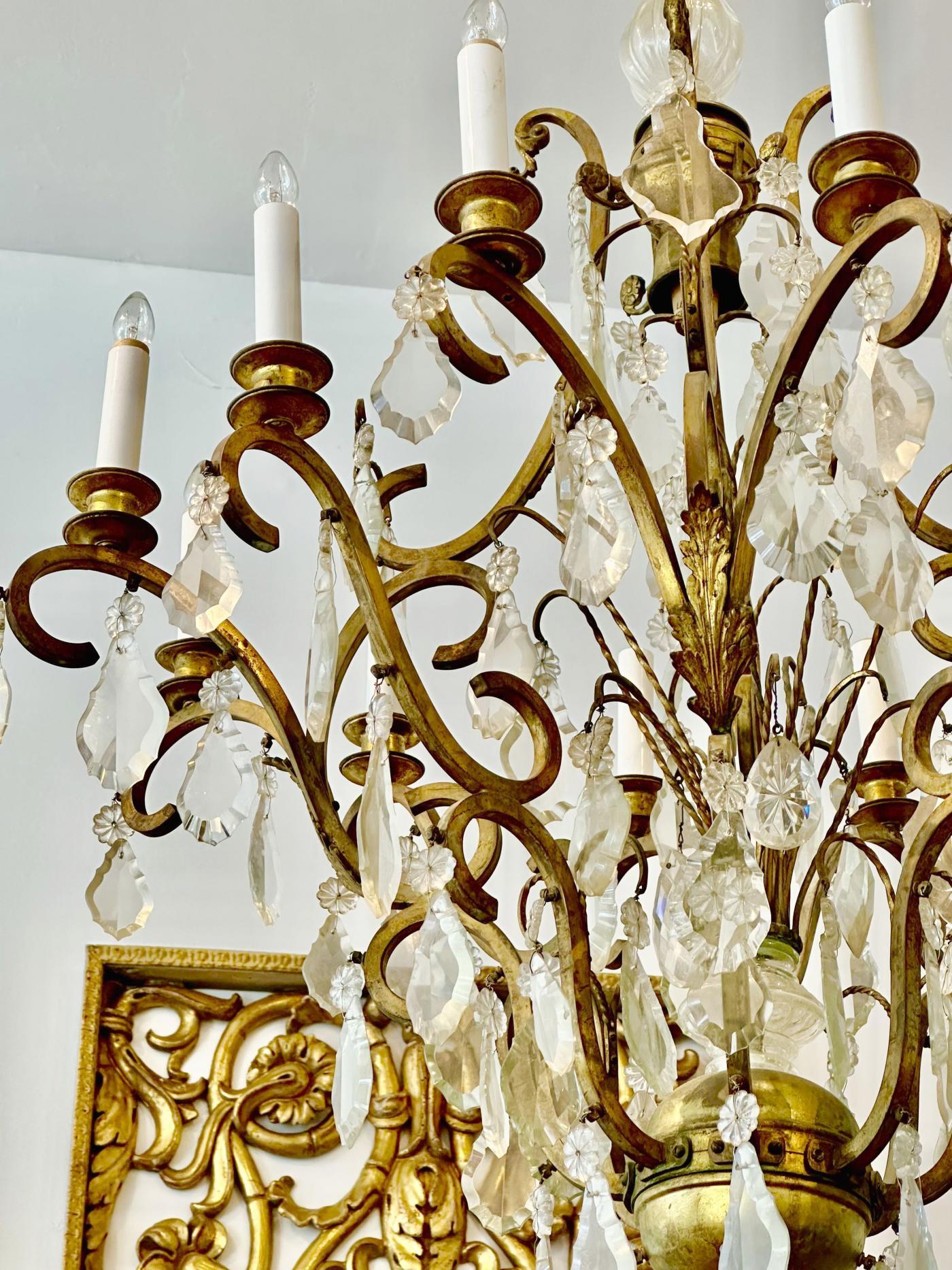 Gabbia vasiforme con bracci a volute e vassoi portacandele, il tutto appeso a gocce di cristallo e prismi sfaccettati.