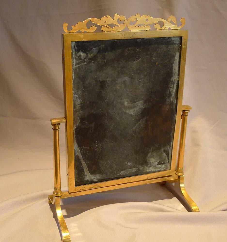Magnifique miroir miniature viennois du 19ème siècle en bronze doré et doré. Posé sur des pieds incurvés, le miroir est maintenu entre des colonnes effilées avec des vis de réglage au sommet et des bases décorées de feuilles et de fléchettes tandis