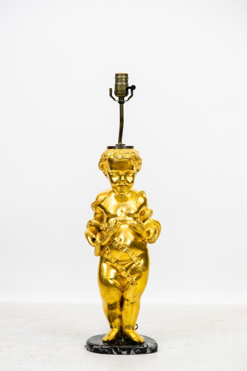 Gilt Cherub lamp holding serpents is on a marble base. It is wired for American use and weighs 24 pounds.    
  