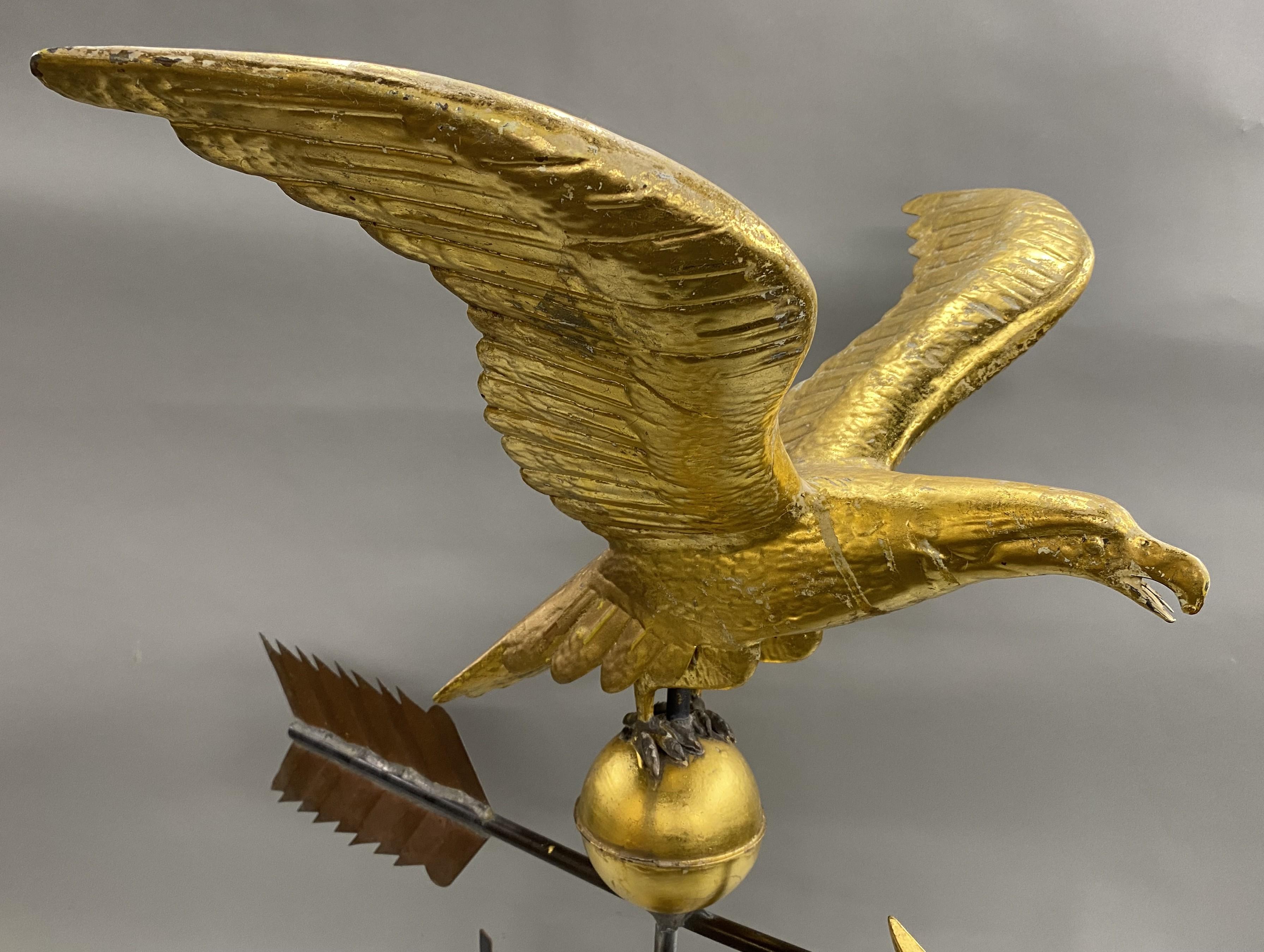 A fine example of an early 20th or late 19th century hollow form gilt copper weather vane with outspread wings, ball, arrow, and directional, mounted on a later round stand, in very good overall condition, with some gilt surface losses, minor dents,