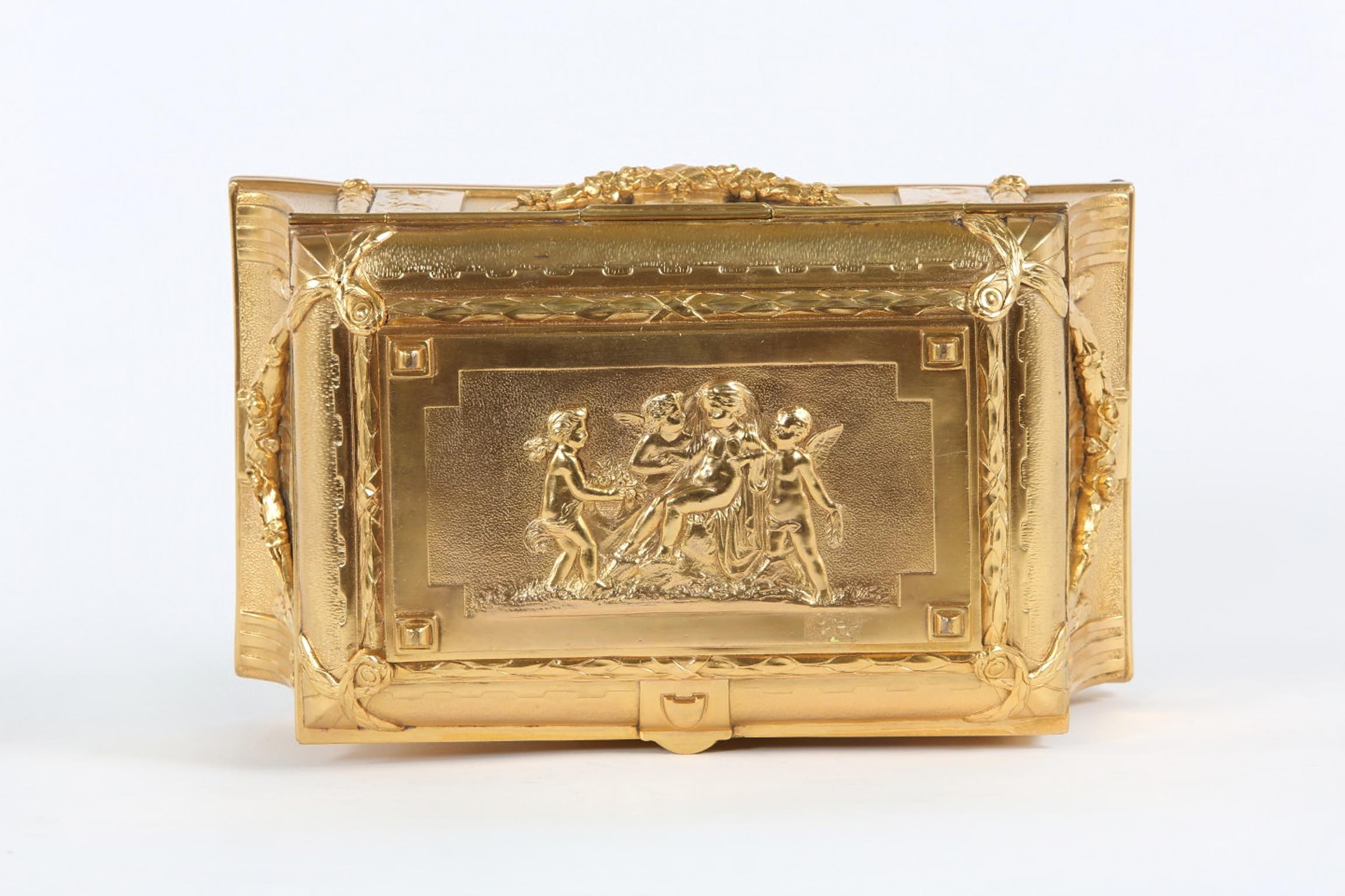 Gilt doré bronze metal footed covered decorated box with exterior floral swags design details and silk interior. Front standing beauties and top cover depiction of seated girl surrounded by putti. Regilded & maker's mark stamped undersigned with