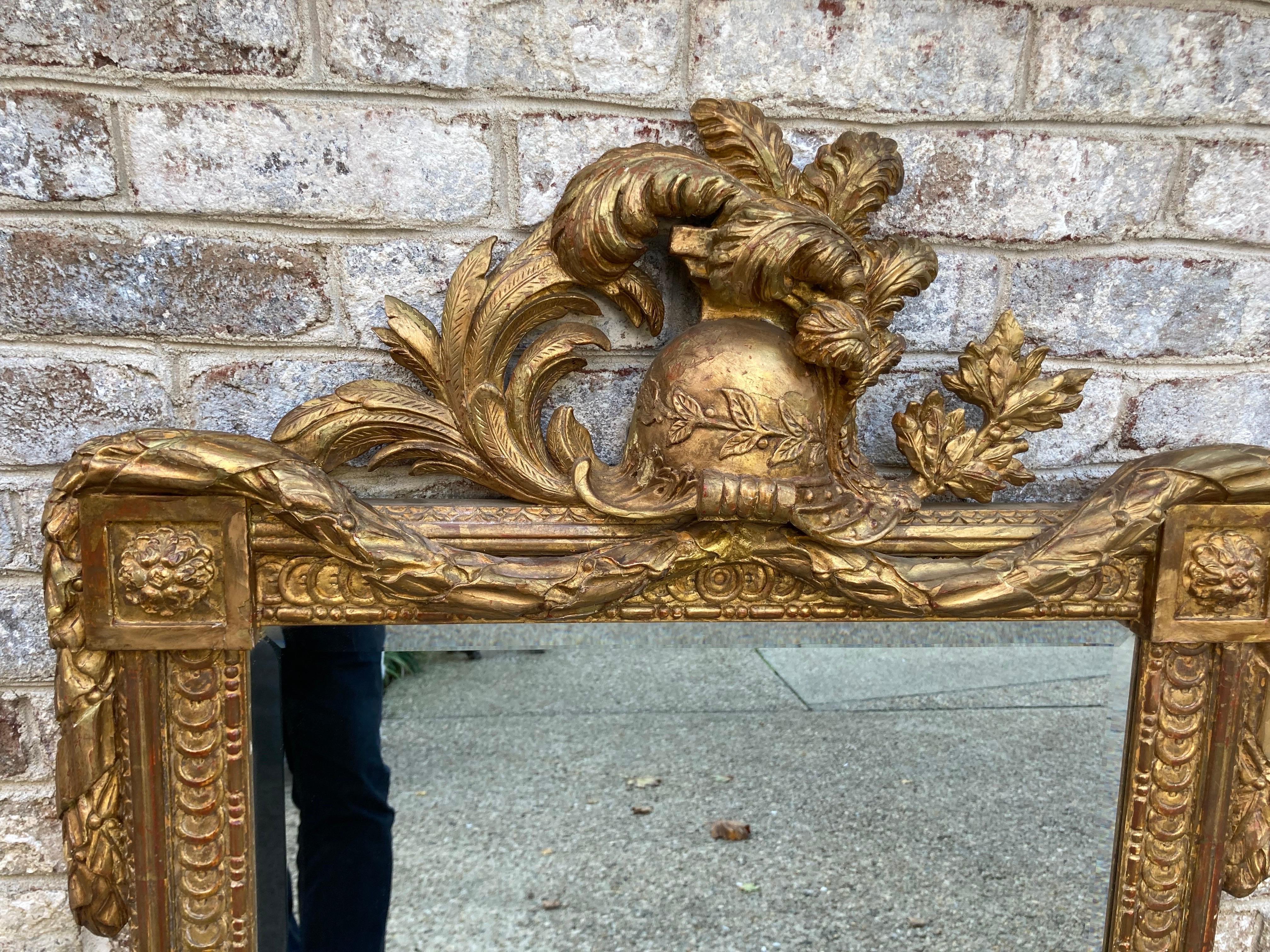 An exceptional and unique French wood carved gilt framed mirror with a helmet and plume. Mirror is beveled.