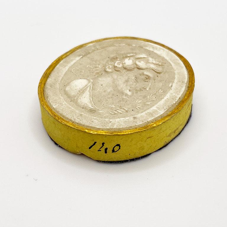 A 19th-century Intaglio Tassie - A seal with the bust of a woman holding an olive branch. Thick gilt paper wrapped around the edge mimicking a frame. There are a few tiny faults in the mold but no damage. A number is penciled in black on the side,