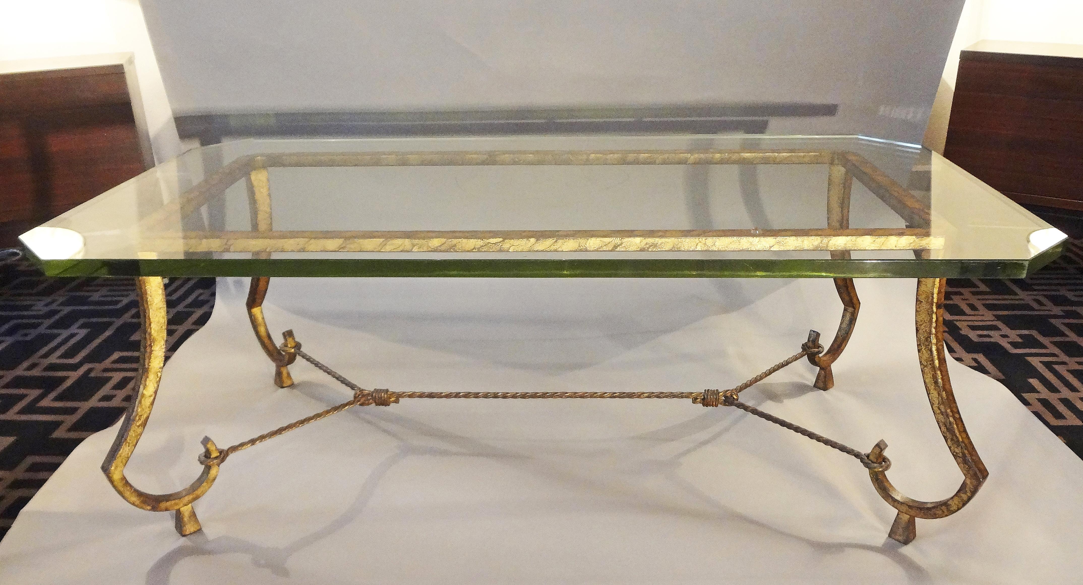 Maison Ramsay, 1950s.
Gilt patinated iron coffee table with glass top.
Rectangular frame resting on four curved legs, on pyramidal sabots.
Refined torsaded cross-bar. Ancient glass top with bevelled corners.
 