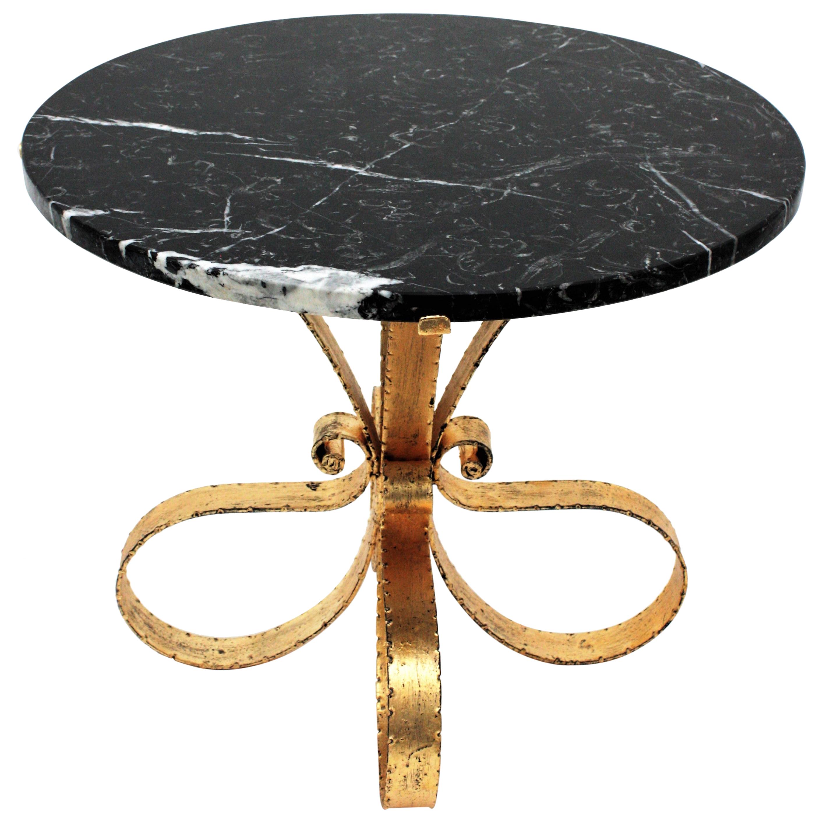 Eye-catching gilt wrought iron low table with round Nero Marquina marble top. Spain, 1940-1950s.
This beautiful drinks table has a marble top with white veins and stands up on a loop design gold leaf gilded iron feet base adorned with scroll