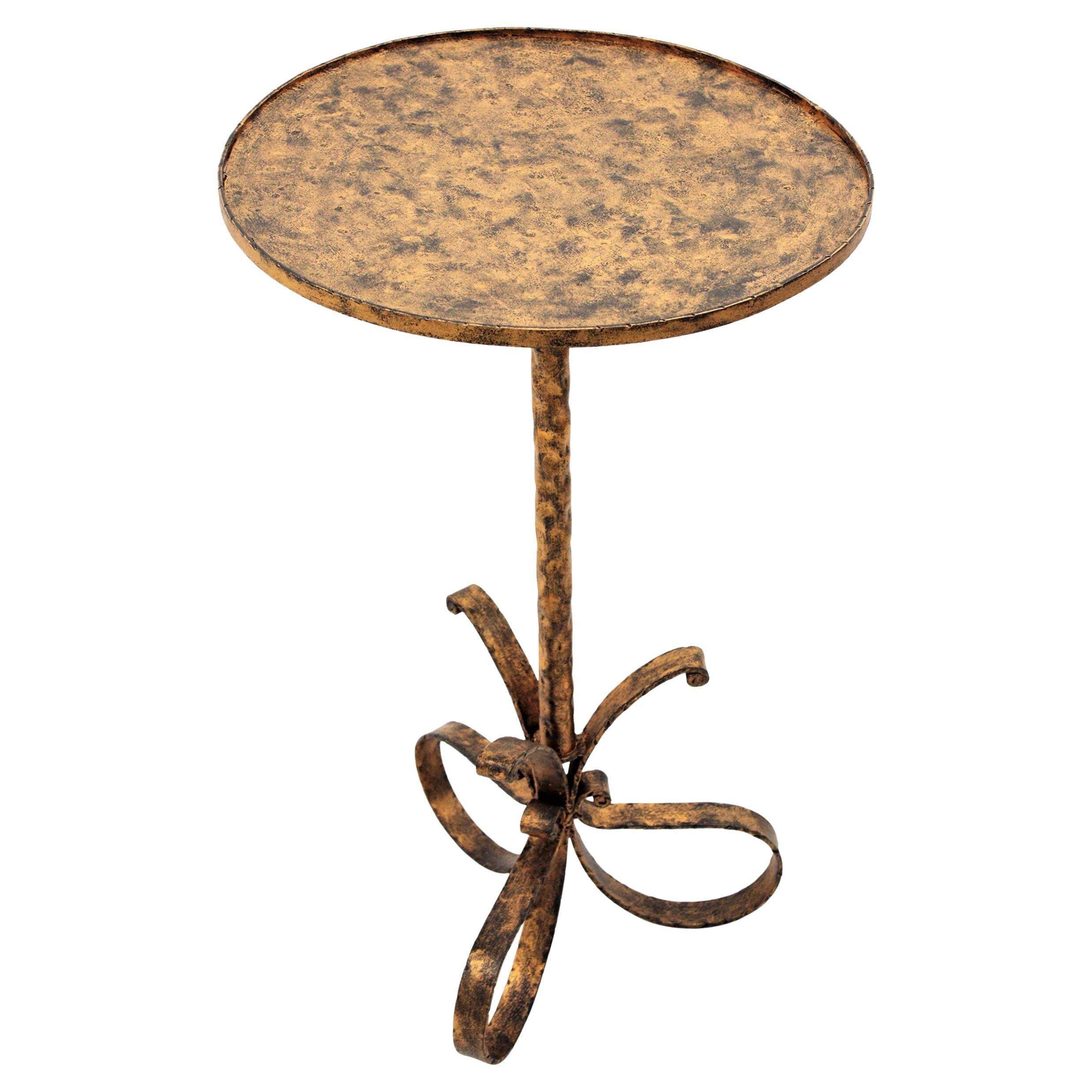 Preciosa mesa auxiliar o de martini, dorada y patinada a mano, con base de lazo de tres patas, España, años 1940-1950.
El tablero es lo bastante grande para usarlo como mesa de centro y se alza sobre una base de hierro en forma de lazo adornada con