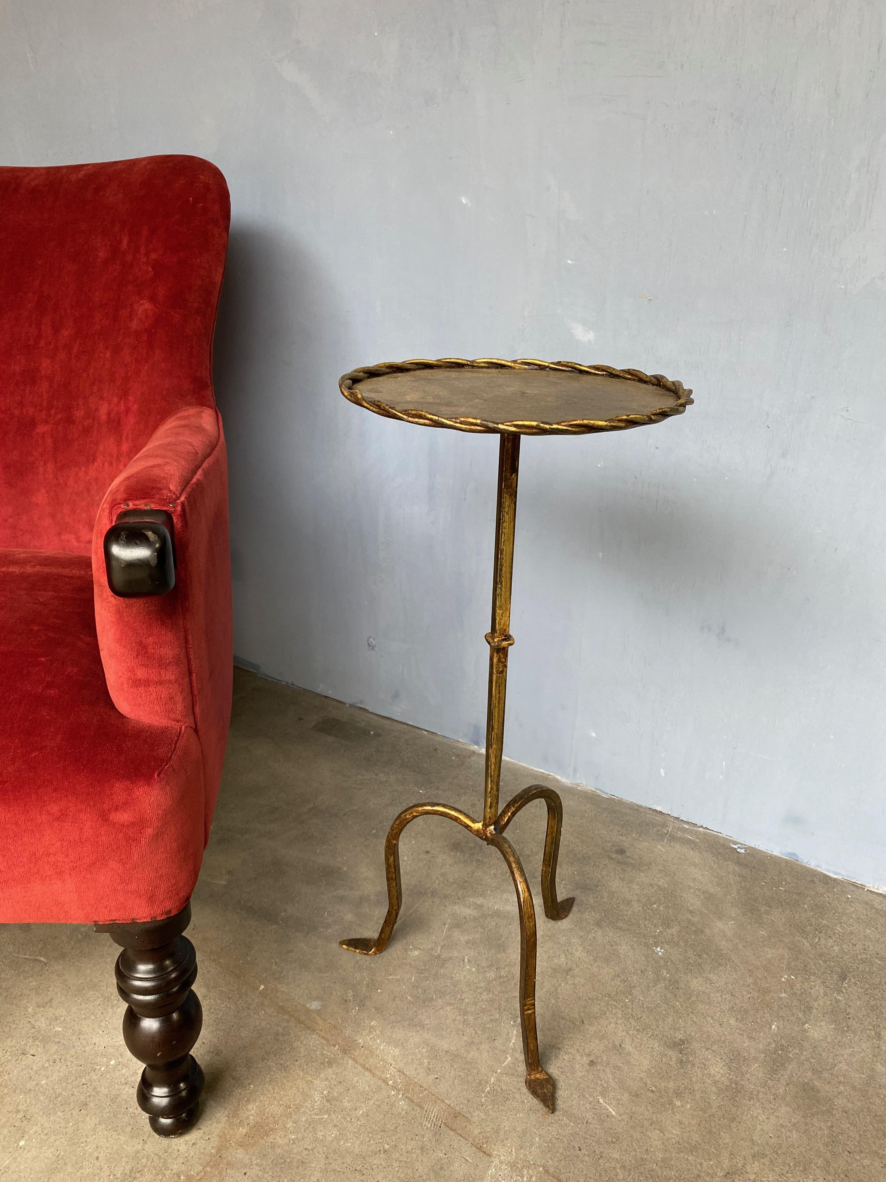A small drink table on a tripod base that will work perfectly as an end table that can be moved around as needed. The table has the original hand applied gold finish with darker undertones, creating a rich and unique finish. The top surface in