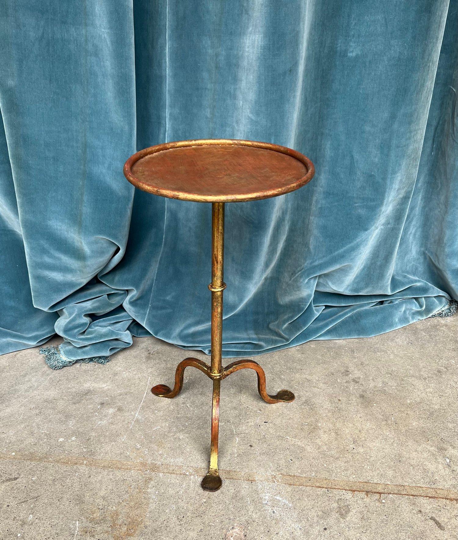 A handsome gilt iron martini table with a beautiful patinated finish. This drinks table is supported by a tripod base. Made from metal and iron, this table is not only practical but also durable and long-lasting. Whether you're looking for a unique