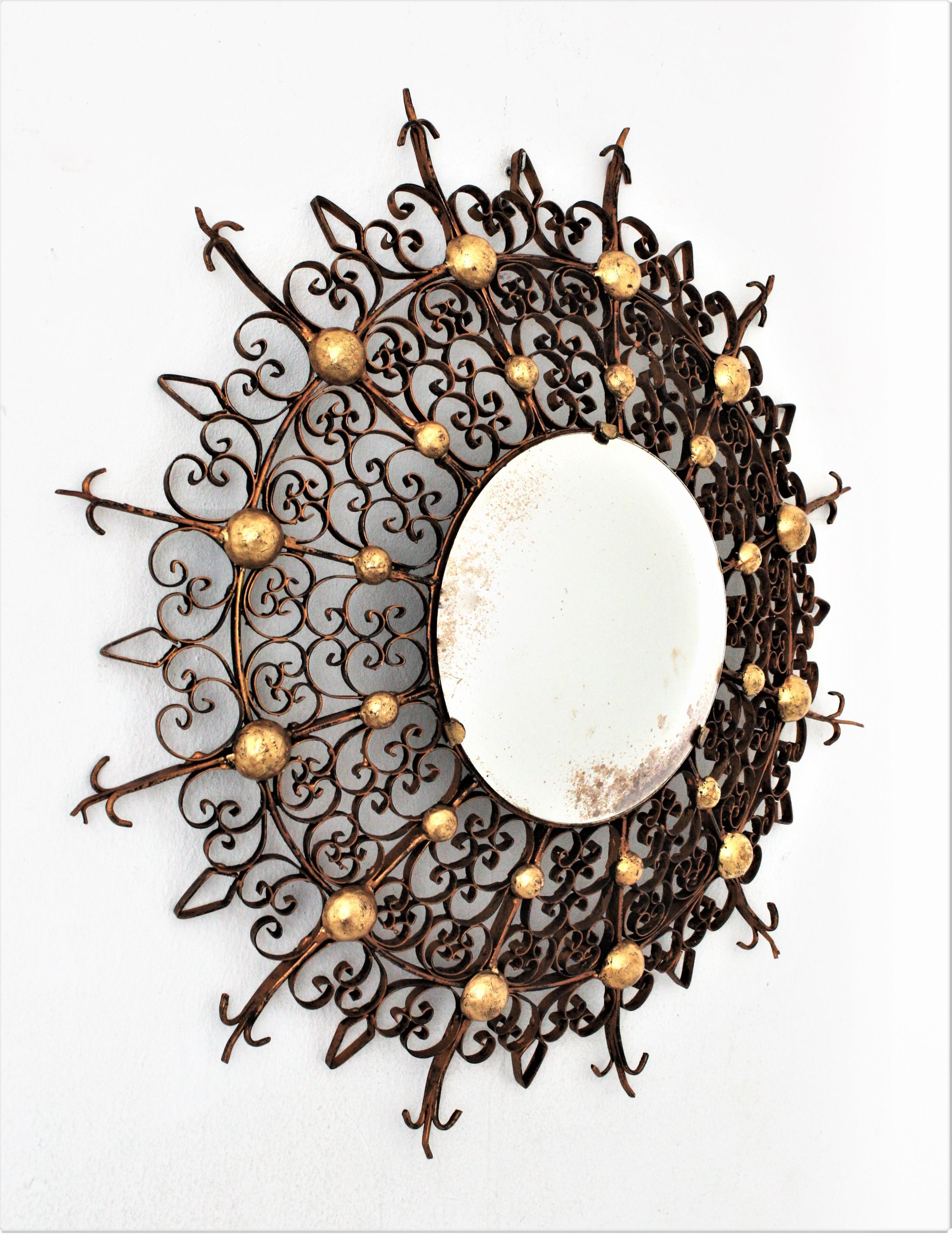 Impressive handcrafted Gothic Revival gilt iron sunburst convex mirror with scroll frame and gilt ball accents. France, 1930s-1940s.
The frame is an intricate filigree decoration with scrolls in diferent sizes accented by gold leaf gilt iron