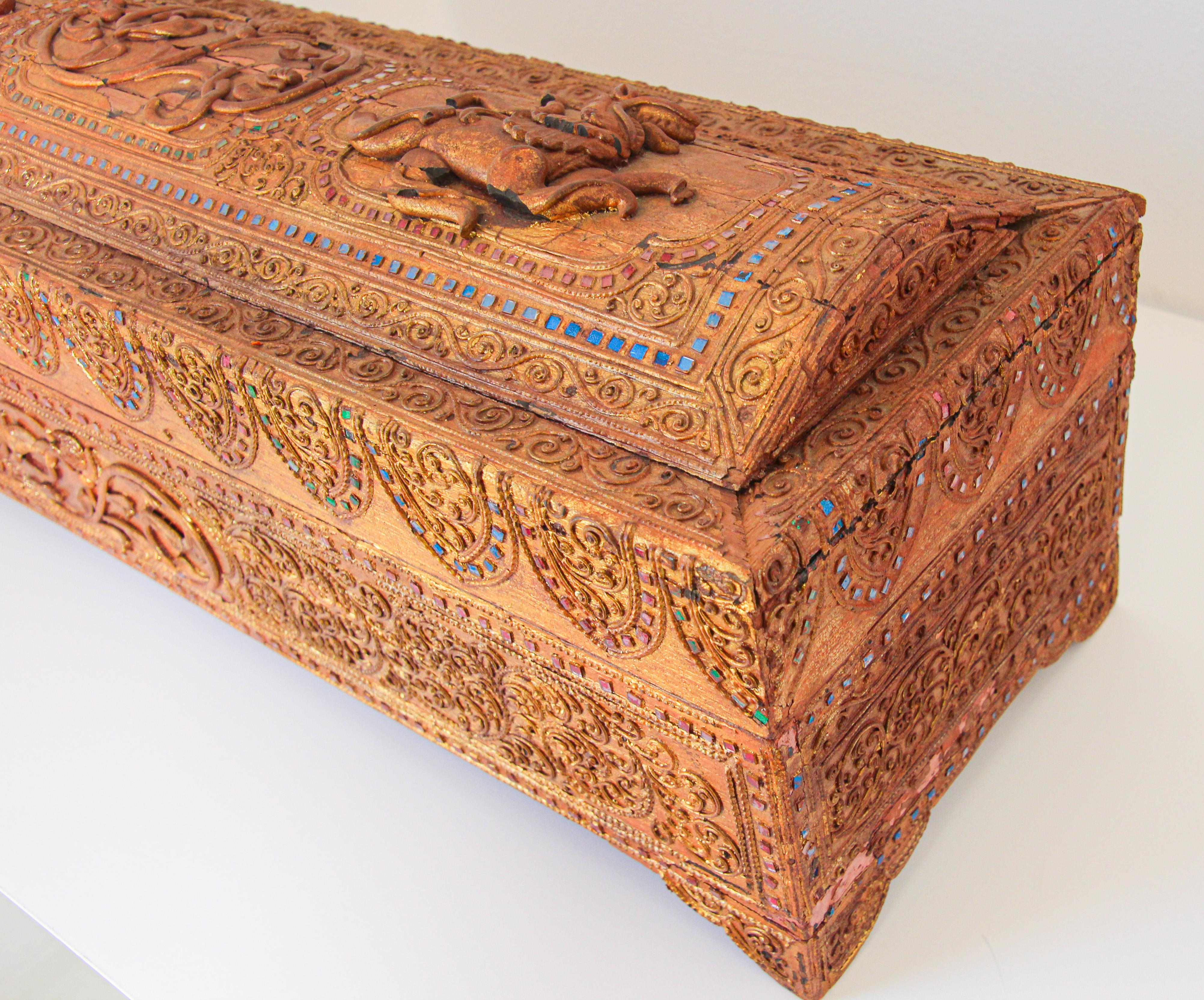 Boîte de rangement pour manuscrits en bois laqué doré Birmanie 19e siècle.
Cette boîte en bois est entièrement recouverte de laque moulée en relief (dite thayo) et de dorure (feuille d'or) et a été incrustée de petits morceaux de verre à fond