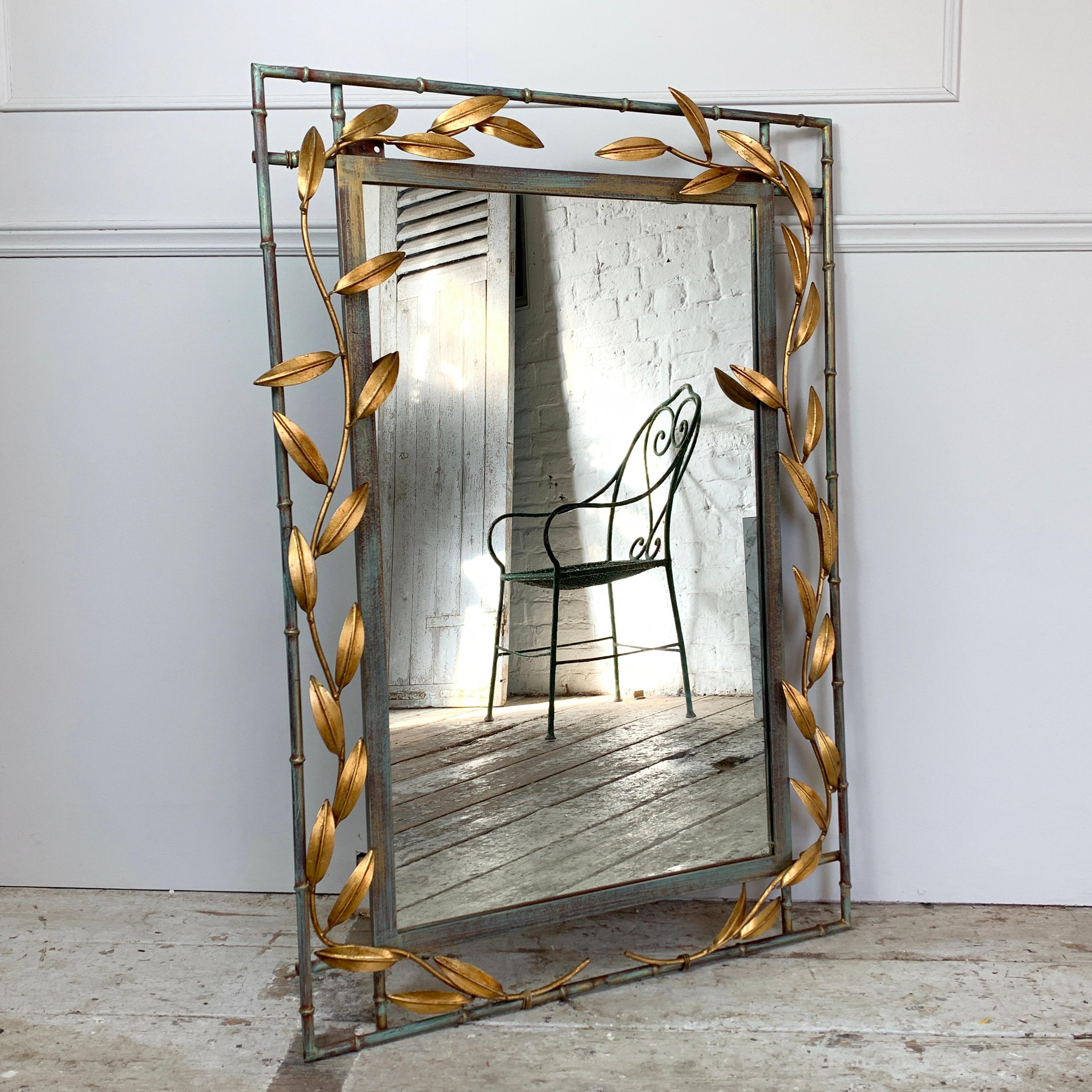 Gilt leaf and faux bamboo mirror
circa 1970s-1980s

Fantastic stems of leaves surround the mirror frame in bright gold leaf finish
The faux bamboo mirror frame itself in metal with mixed tones of color to the finish
There are hanging hooks to the