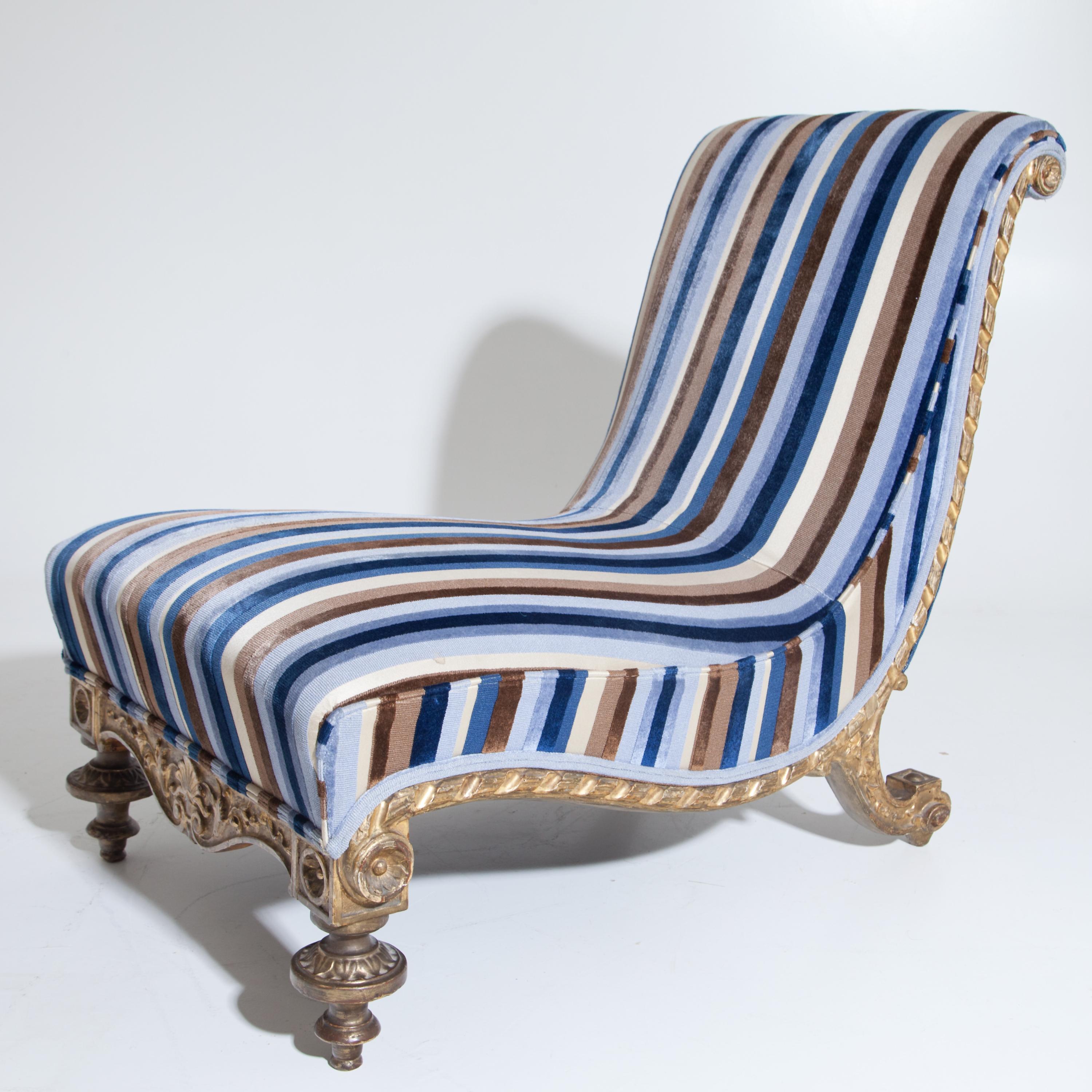 Low lounge chair on baluster legs in front and curved feet in the back. The S-shaped curved seat is covered with striped fabric. The frame is carved and golden patinated.
  