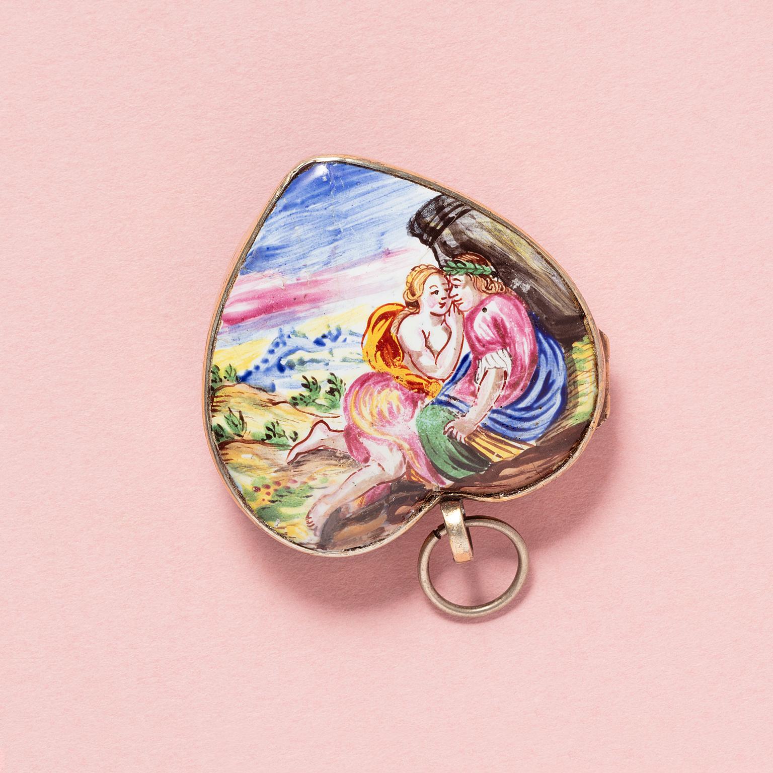 A large heart-shaped pendant made of gilt metal and enamel, one side of the heart depicts Apollo with one of his lovers, and the reverse shows a basket filled with burning hearts, accompanied by a banner bearing the inscription 