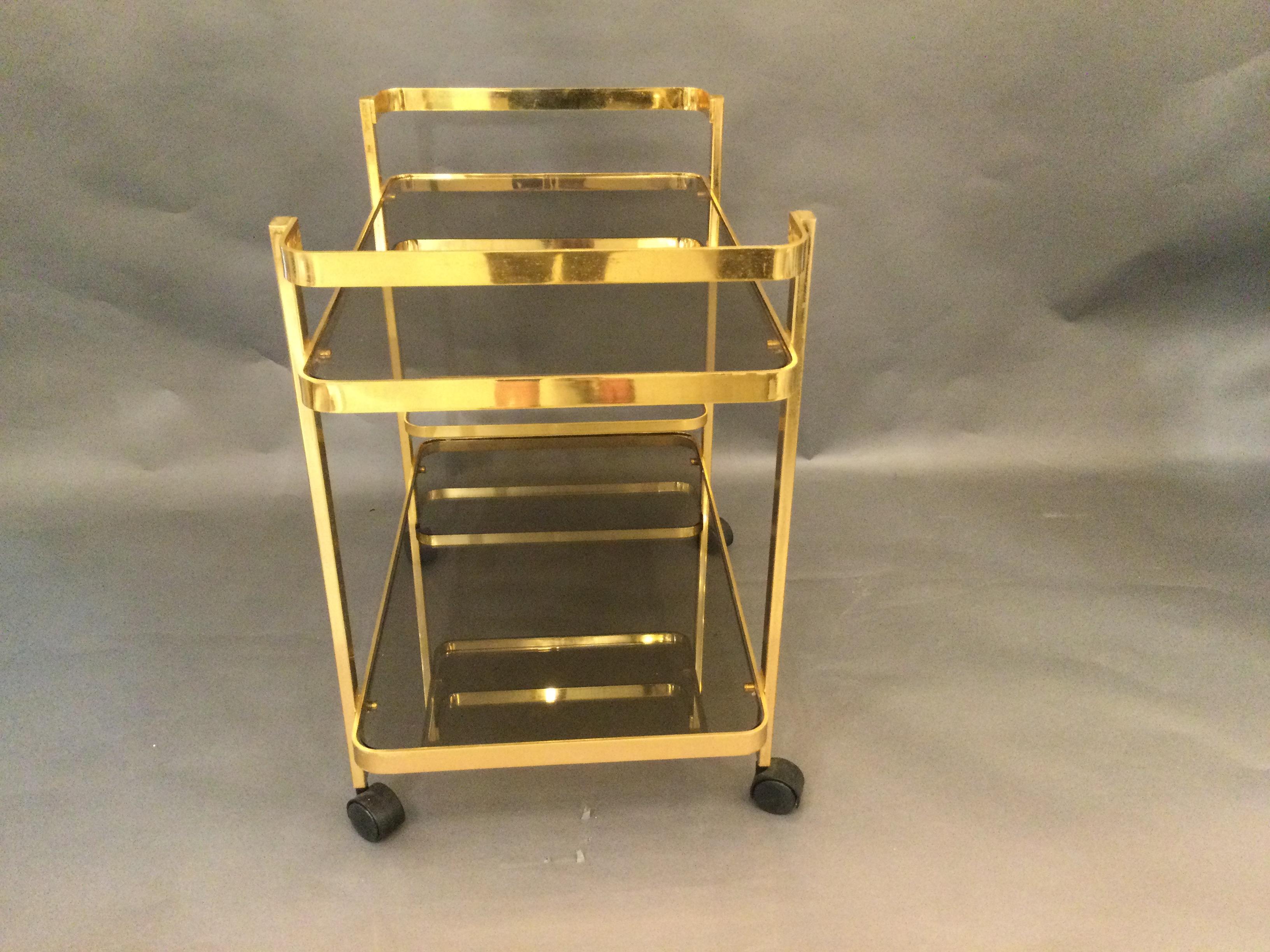 Elegant drinks trolley/bar cart in gilt metal with two smoky glass. Shelves are surrounded by simple curved gilt metal frame extending on the top shelves to create a handle at both ends. Bottle holder holds up to three bottles. Designed in the 1970s