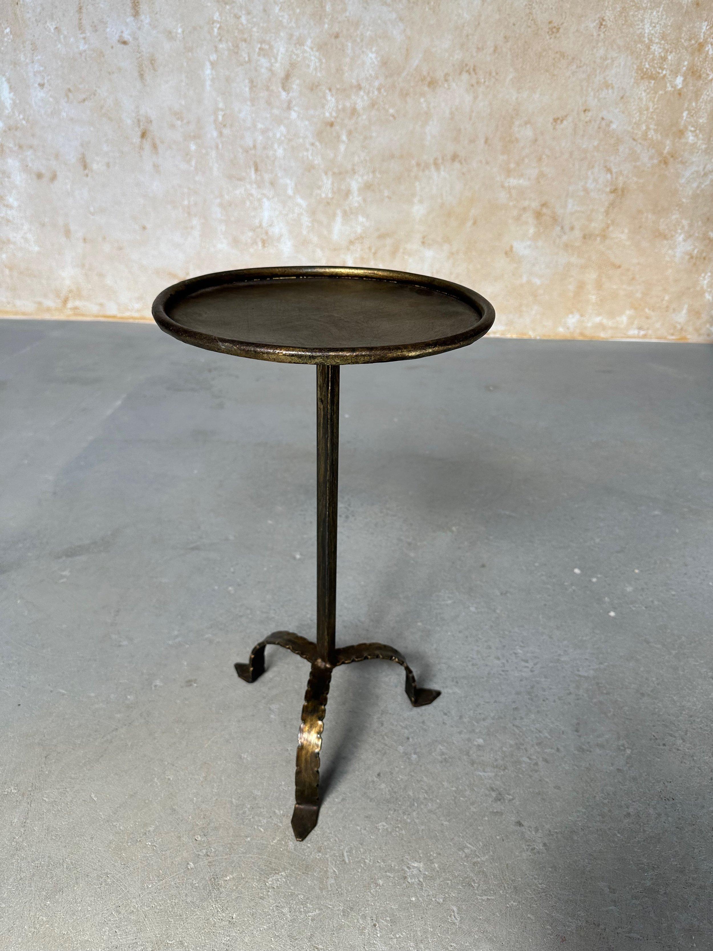 This unique small Spanish end table was recently crafted by accomplished artisans using traditional iron-working methods and features an elevated hammered tripod base with pointed feet. The hand-applied gold patina has subtle dark undertones and the