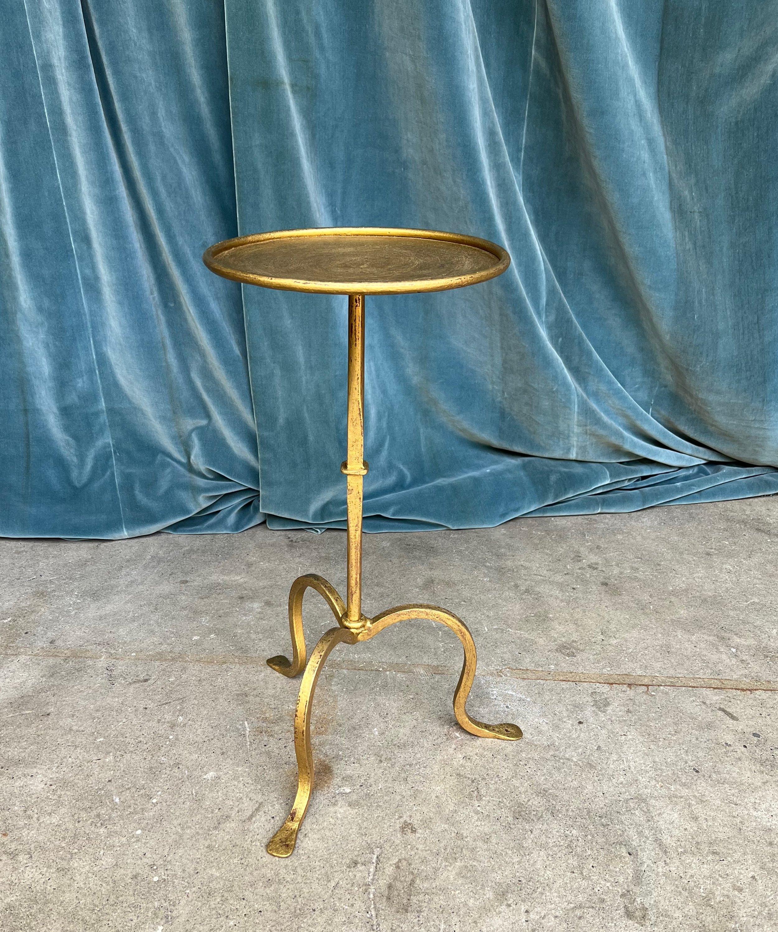 This small scaled  beverage table, meticulously hand-forged in Spain, is a captivating and functional item of furniture. Its sturdy tripod foundation, combined with an unusual ring motif on the shaft, ensures solid stability while also offering an