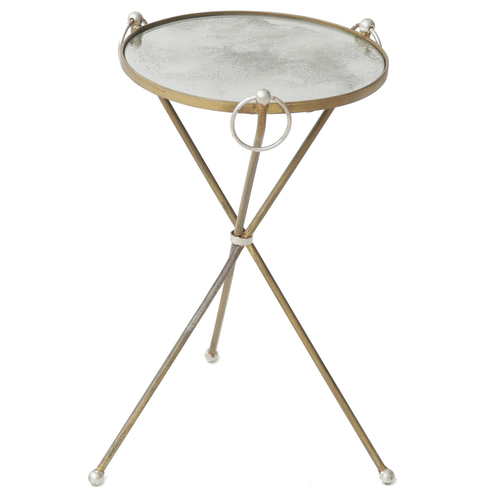 Accent table in the manner of Jean Michel Frank, of silver and gold gilt metal, having a round top of aged mirrorplate, raised on a tripod of iron legs with ball feet, joined by a central loop, decorated at the top by a trio of ring ornaments.